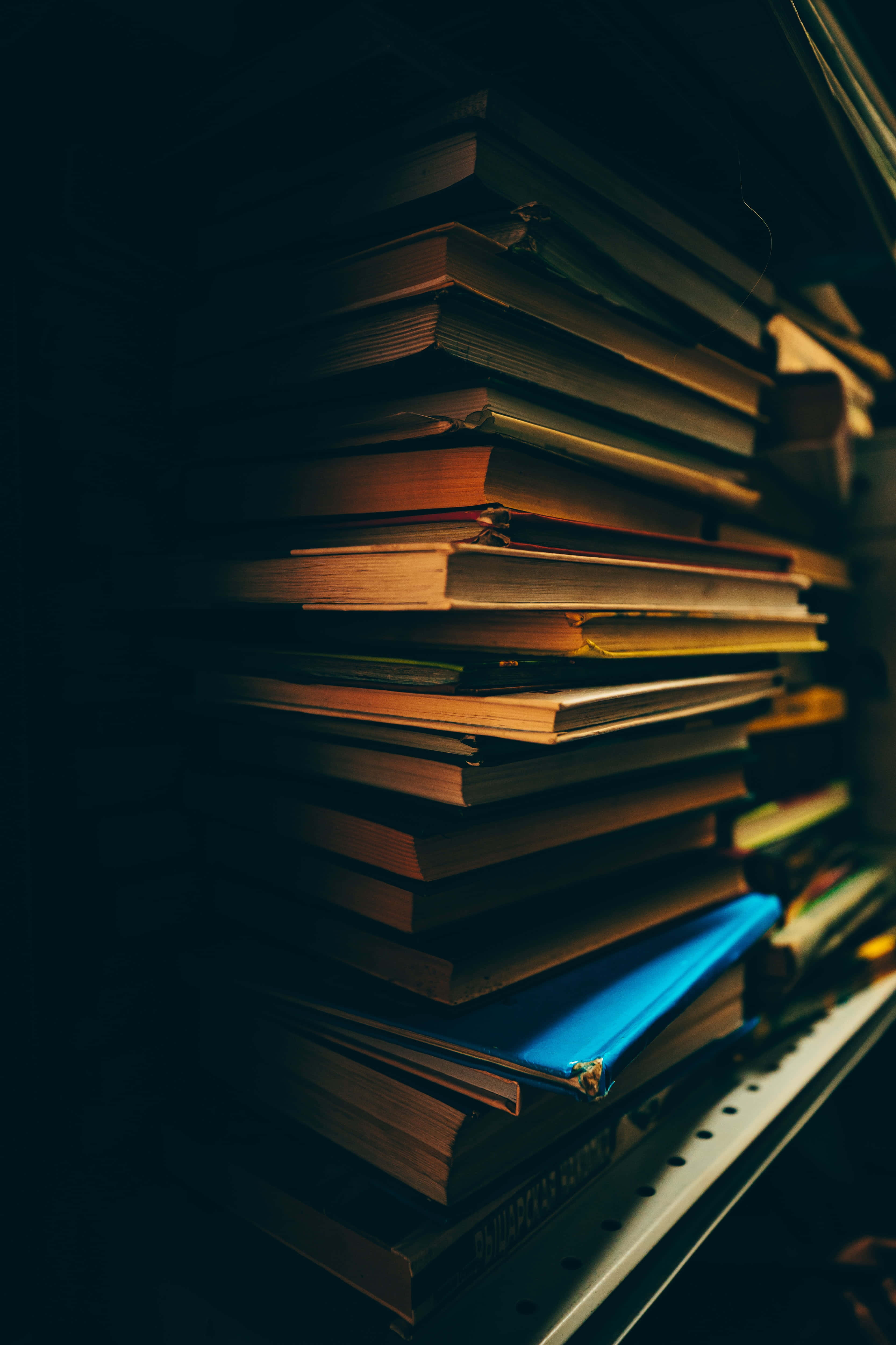 books 桌布 壁紙 — 一堆高高的書本放在書架上，沐浴在溫暖的金色光芒中，背景昏暗。