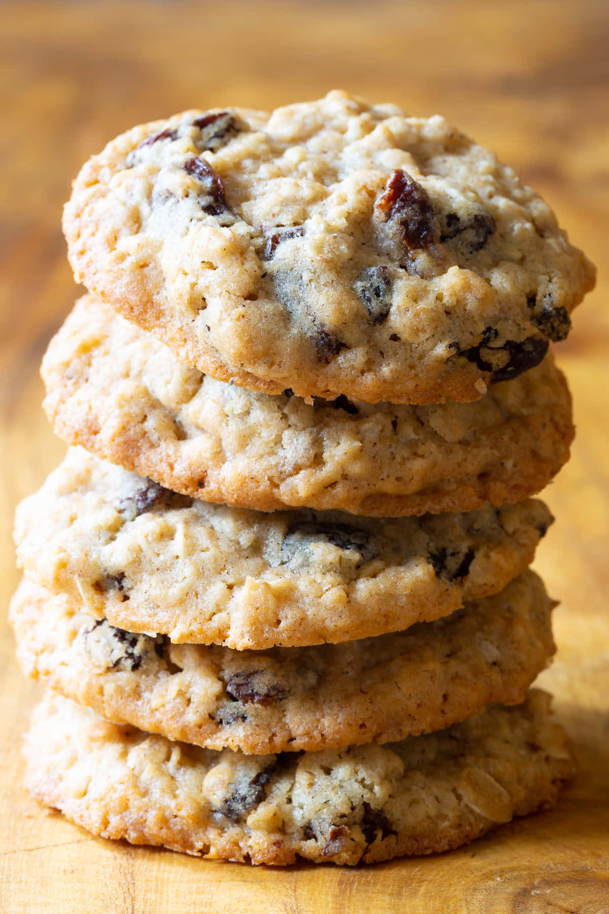Cookie 桌布 壁紙 — 一堆高高的溫暖金黃色燕麥葡萄乾餅乾，可見燕麥片和飽滿的葡萄乾，誘人地放在木質表面上。