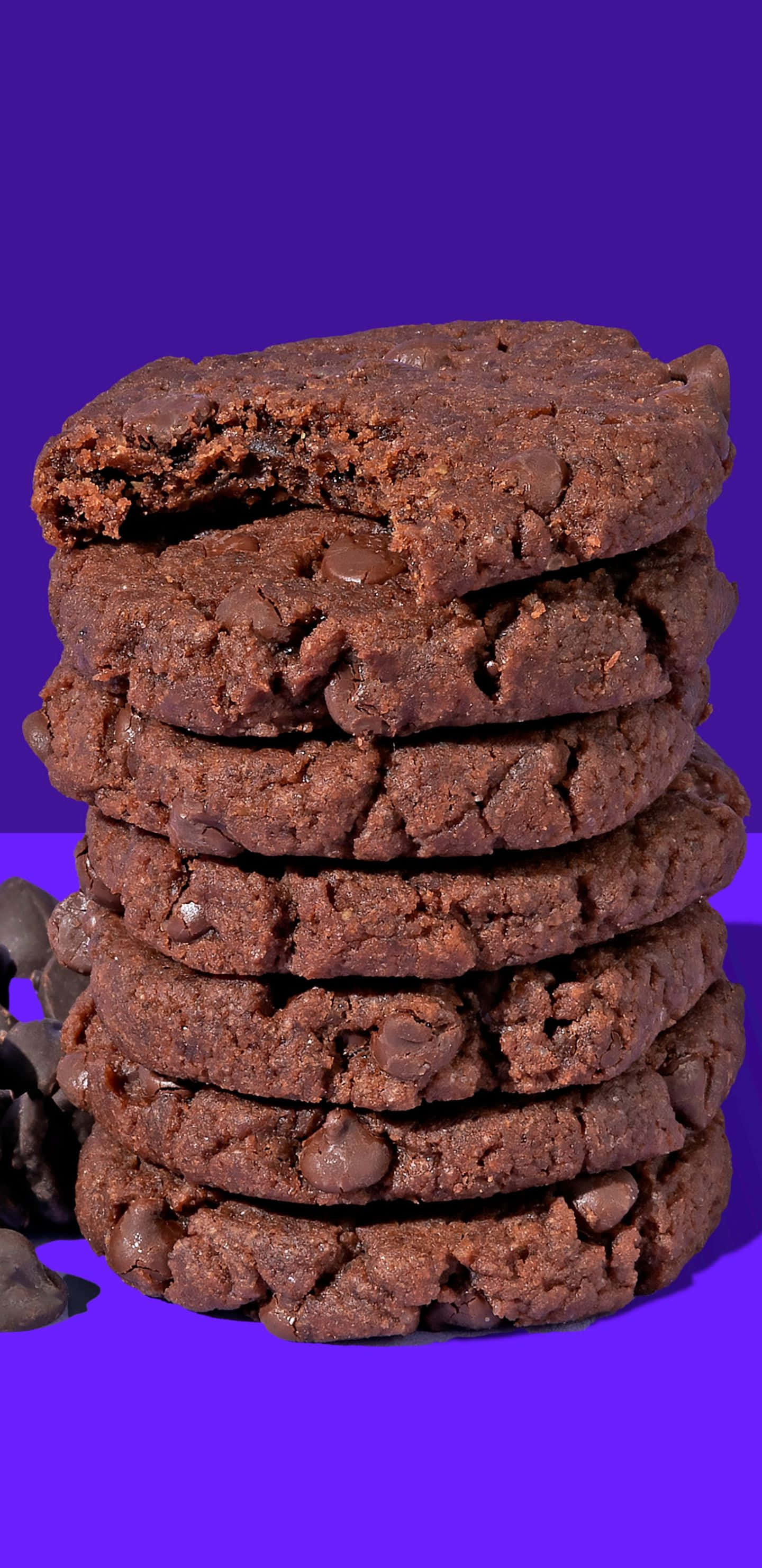 Pixel 3xl Cookies 桌布 壁紙 — 一堆高高的濃郁巧克力餅乾，頂部餅乾碎裂，露出黏稠的內部，背景為鮮豔的紫色。