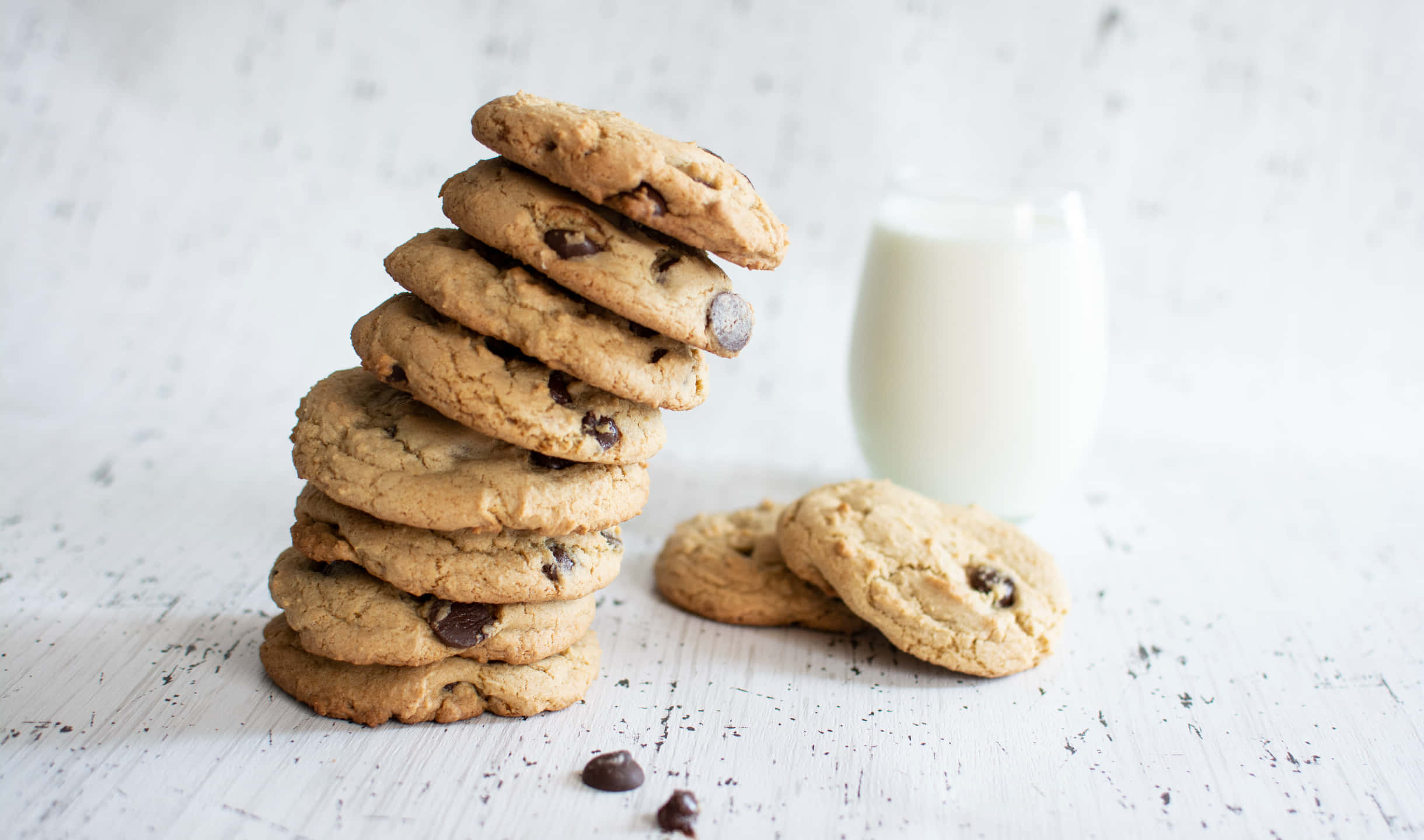 Cookies 桌布 壁紙 — 一堆高高的金黃色巧克力曲奇，旁邊放著一杯牛奶，放在白色紋理表面上。