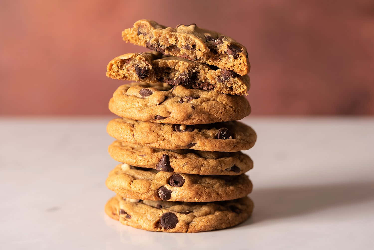 Cookie 桌布 壁紙 — 一堆高高的金黃色巧克力餅乾，其中一塊折成兩半，露出黏稠的融化巧克力。