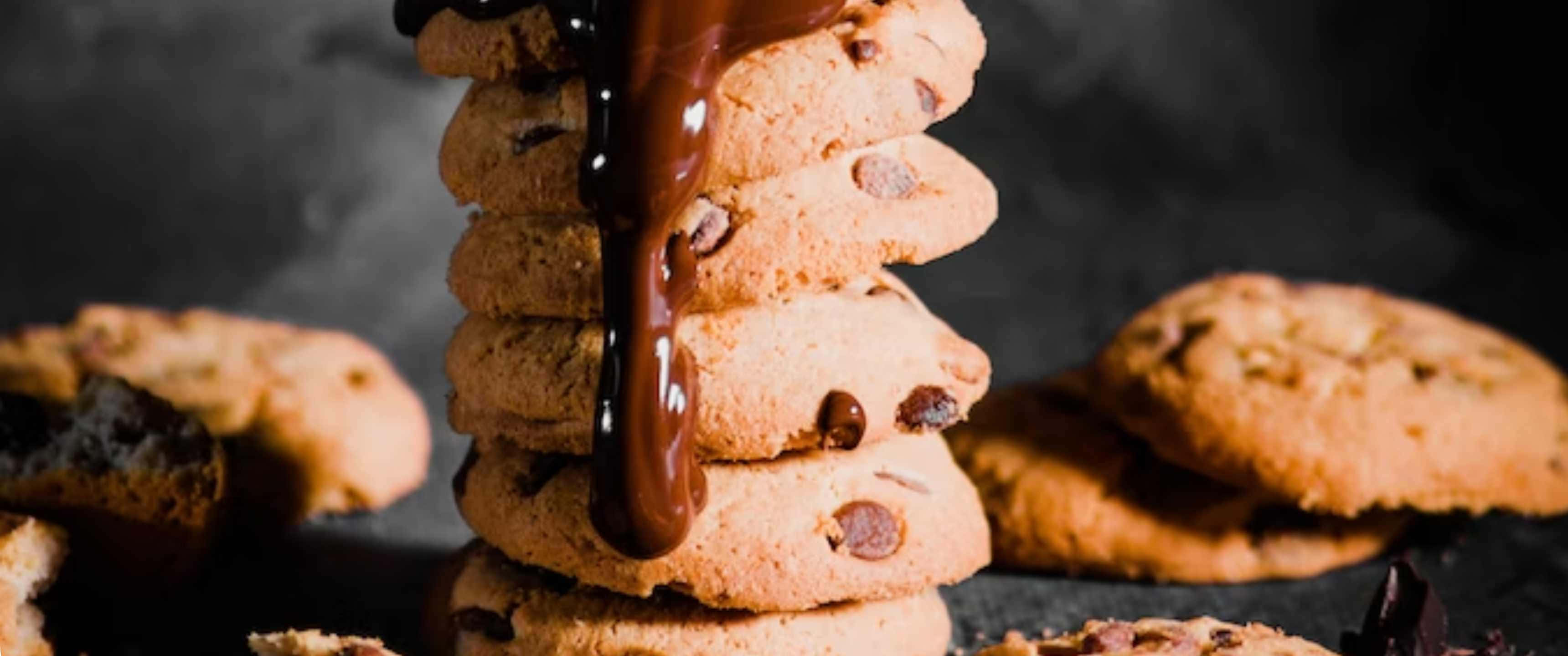 Cookies 桌布 壁紙 — 一堆高高的金黃色巧克力餅乾，濃郁的融化巧克力沿側邊滴落，襯托著陰暗的氛圍背景。