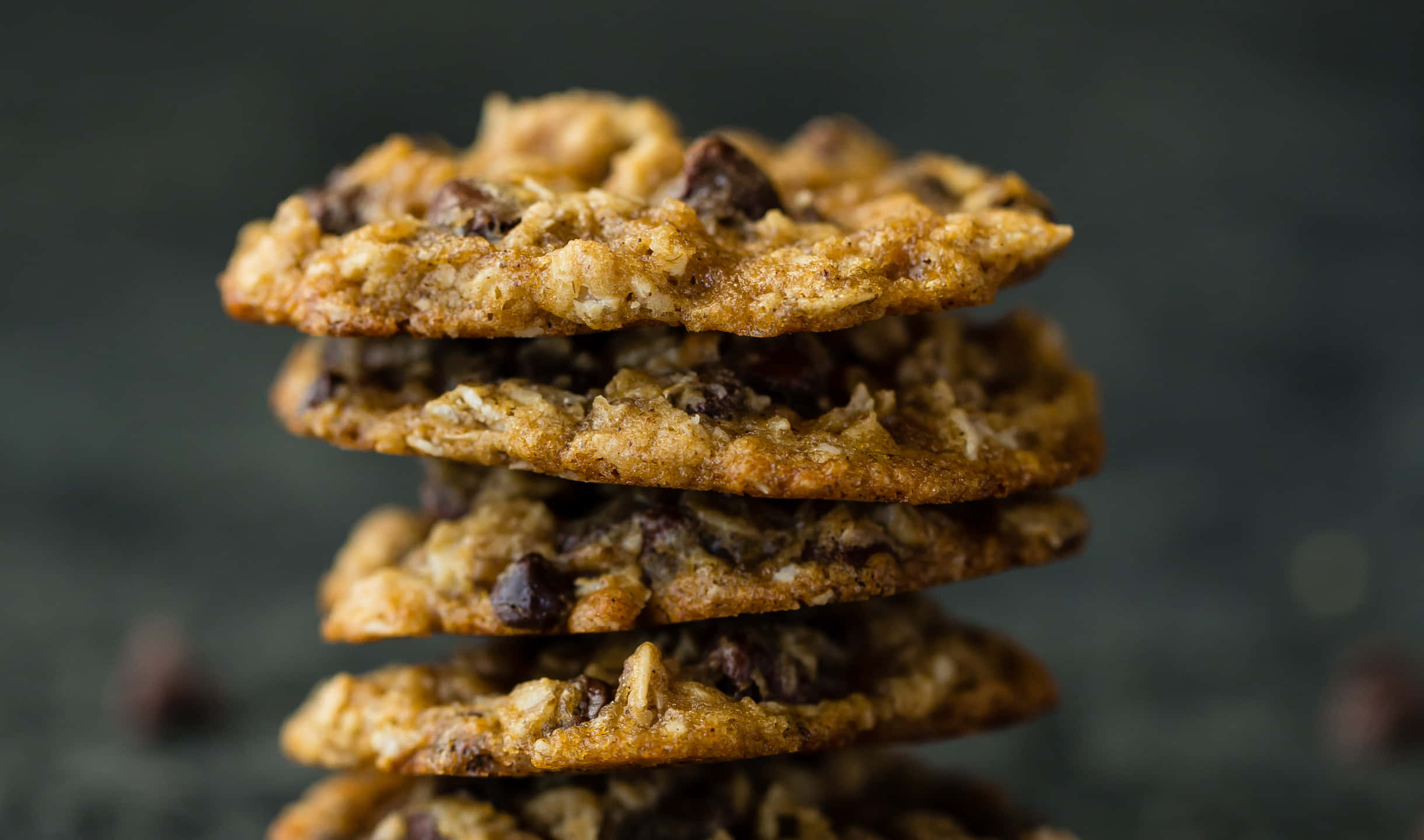 Cookies 桌布 壁紙 — 一堆高高的金黃色燕麥巧克力餅乾，可見塊狀，背景柔和模糊深色。