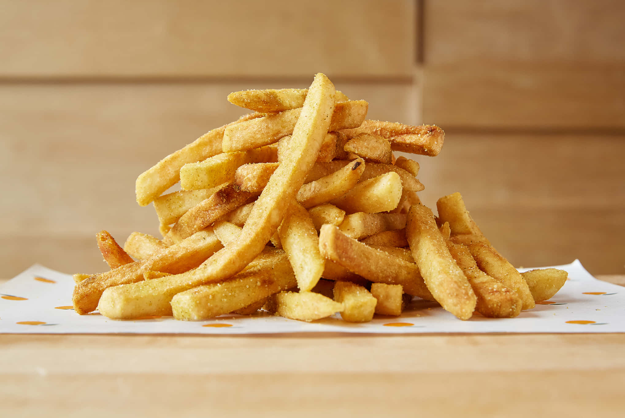 French Fries 桌布 壁紙 — 一堆高高的金黃酥脆調味薯條放在圖案紙上，背景是溫暖的木質。