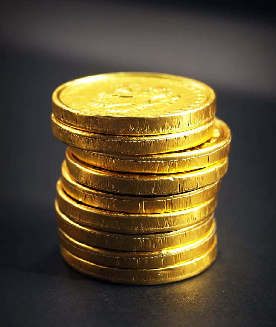 金錢 桌布 壁紙 — 一堆高高的閃亮金色包裝巧克力金幣在柔和光線下於深色背景上閃閃發光。