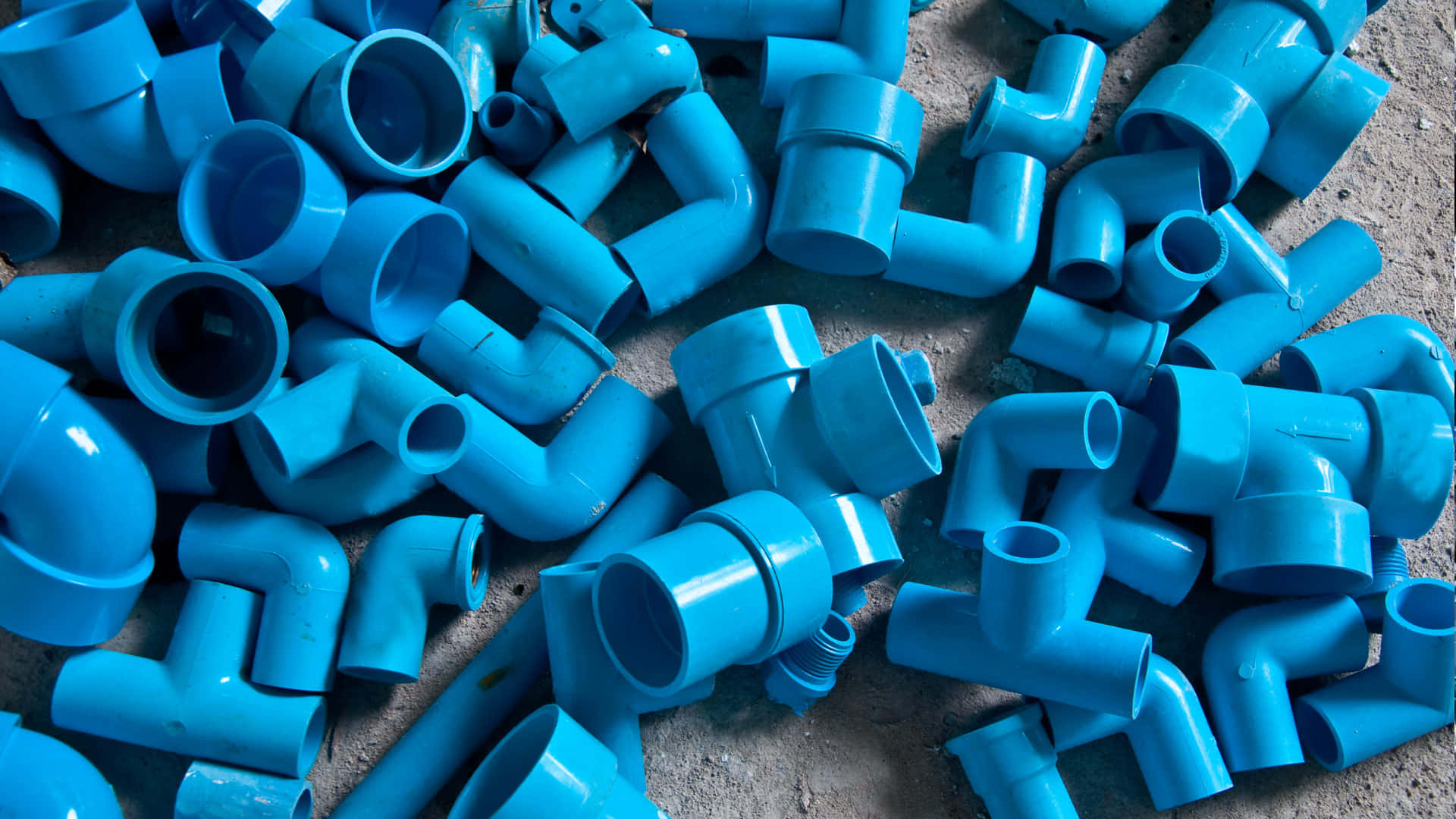 Plumbing 桌布 壁紙 — 一堆鮮豔亮藍色塑膠管件散落在粗糙的混凝土表面上。