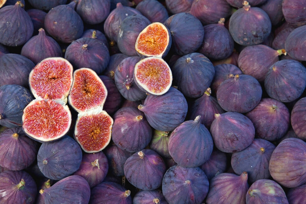 Fruits 桌布 壁紙 — 一堆鮮豔的成熟紫色無花果，其中幾個切半露出多汁的粉紅色內部。