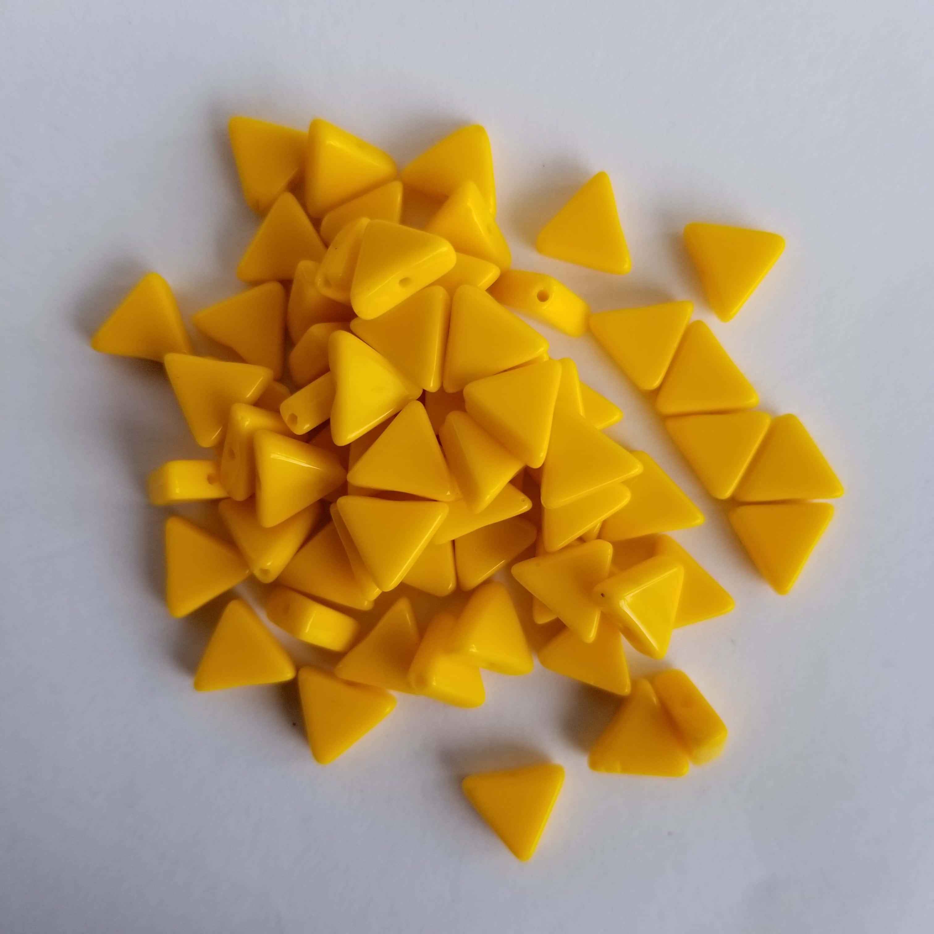 Yellow Triangle 桌布 壁紙 — 一堆鮮黃色三角形塑料珠子散落在純白色表面上。