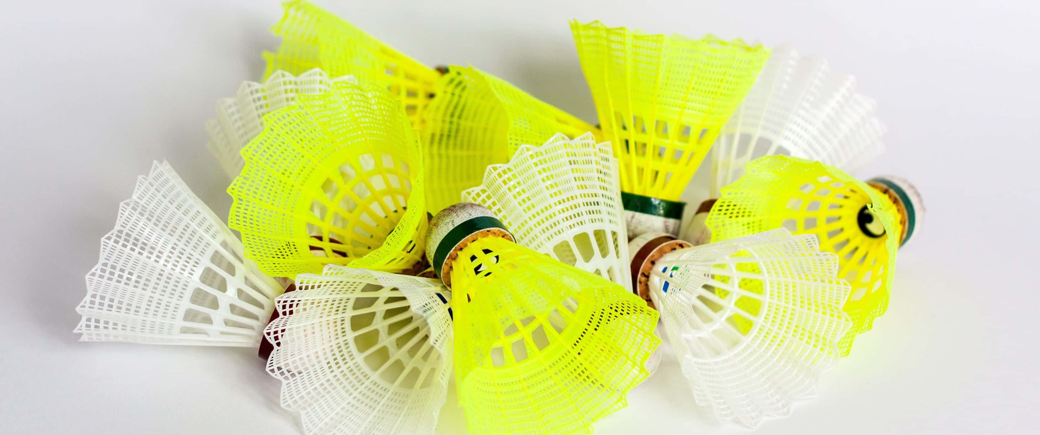 3440x1440p Badminton 桌布 壁紙 — 一堆鮮黃色和白色的羽毛球散落在乾淨的白色表面上。