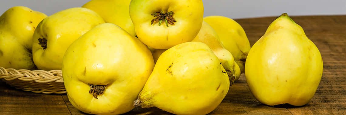 Quince 桌布 壁紙 — 一堆鮮黃色的榲桲，表皮有紋理，放在一個鄉村風格的木桌上，旁邊有個編織籃。