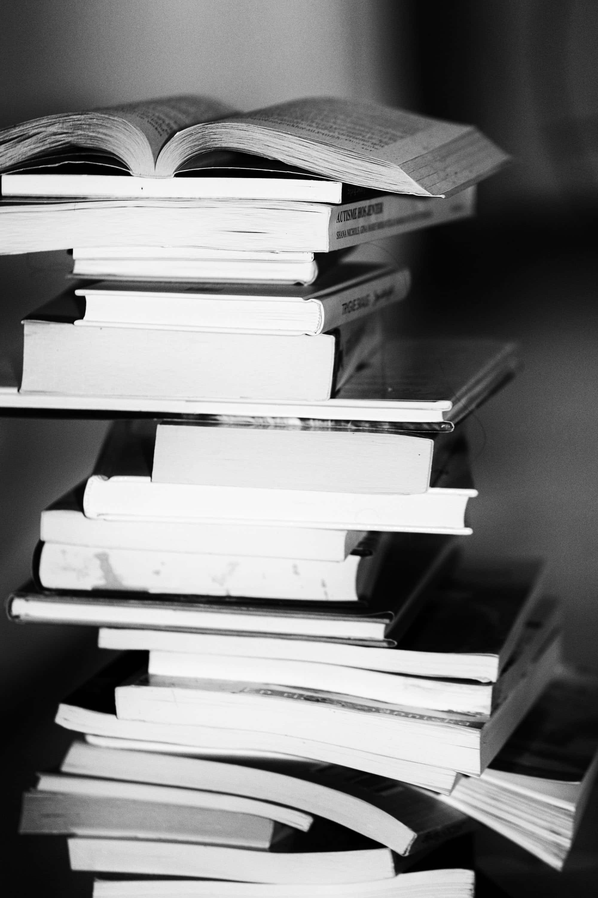 Black And White Book 桌布 壁紙 — 一堆黑白書籍搖搖欲墜地疊得很高，頂部有一本打開的書露出文字。