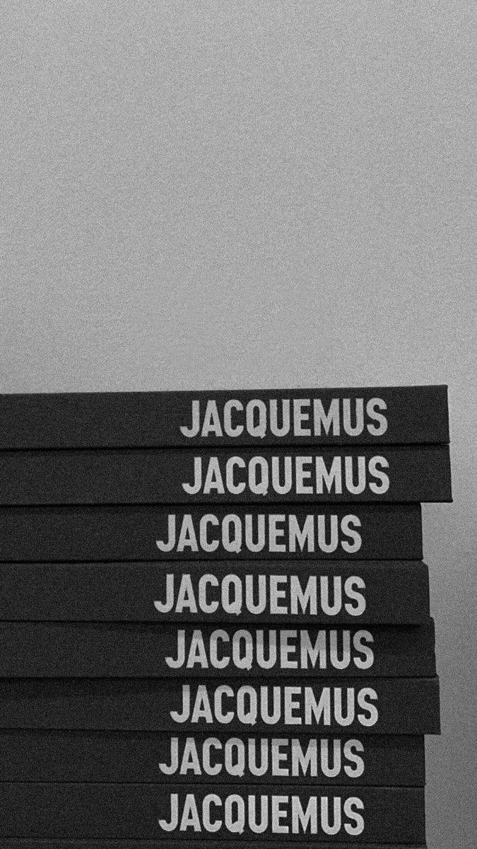 品牌 桌布 壁紙 — 一堆黑色書籍，上面有白色 'JACQUEMUS' 文字，背景為紋理灰色。