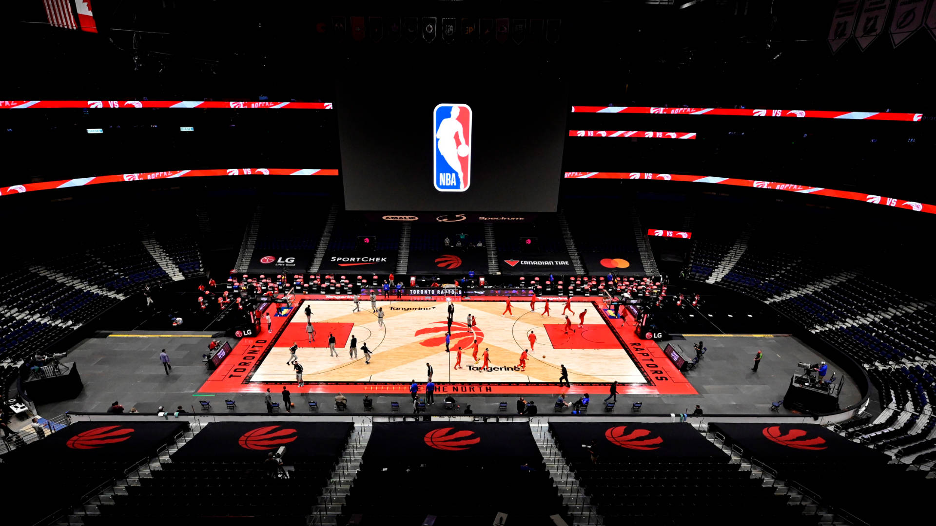 Raptors 桌布 壁紙 — 一場NBA籃球比賽在明亮的場館燈光下展開，球員在拋光球場上移動，周圍是空座位。