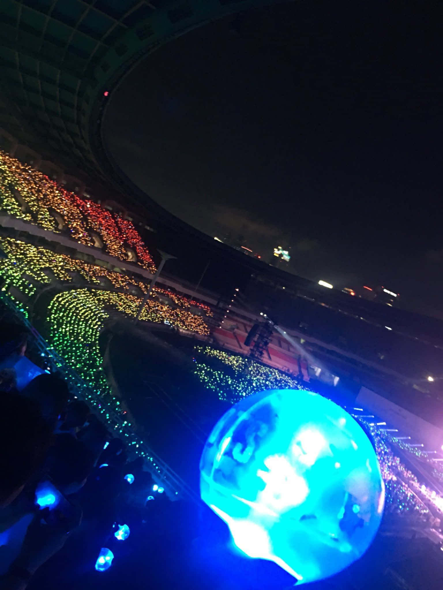 Bts Army Bomb 桌布 壁紙 — 一場令人眼花撩亂的夜間演唱會，粉絲們手持發光燈光，在巨大的體育場中形成色彩繽紛的圖案。