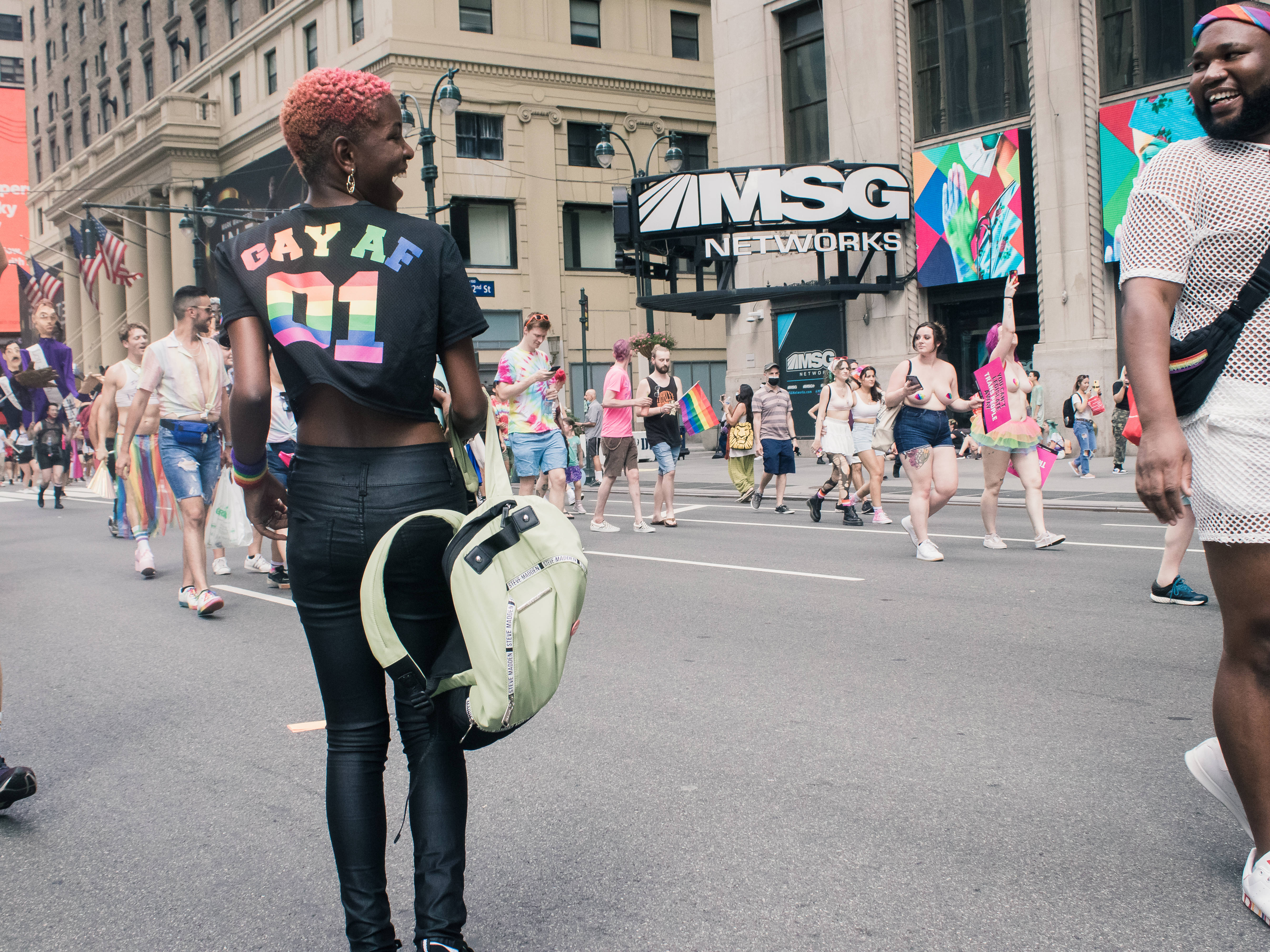 女同志 桌布 壁紙 — 一場充滿活力的Pride遊行擠滿了城市街道，參與者歡快地揮舞彩虹旗，穿著色彩繽紛的服裝，在明亮的日光下。