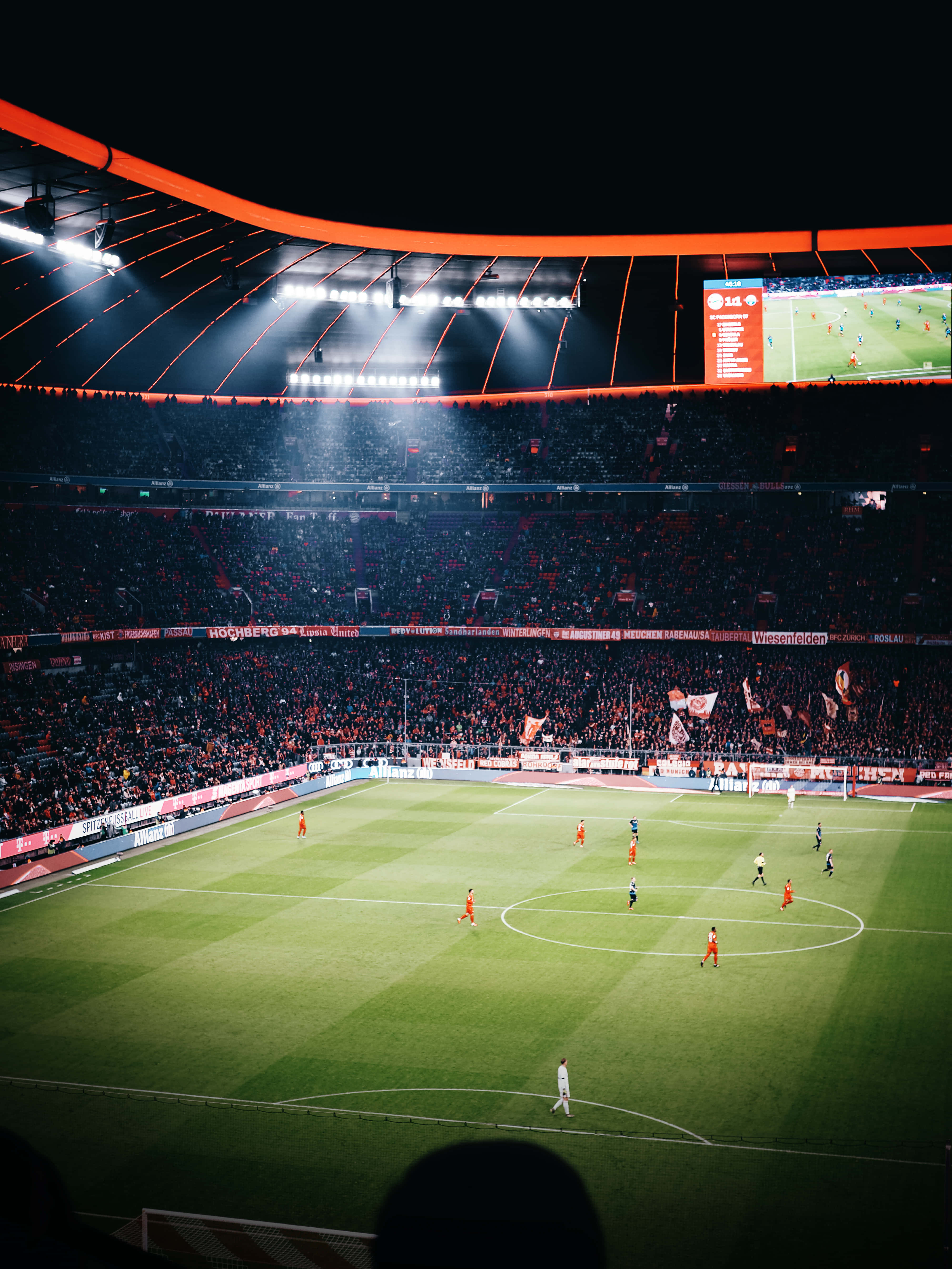 Soccer Stadium 桌布 壁紙 — 一場充滿活力的夜間足球比賽在明亮的體育場燈光下展開，球迷在擠滿的場館中揮舞旗幟。