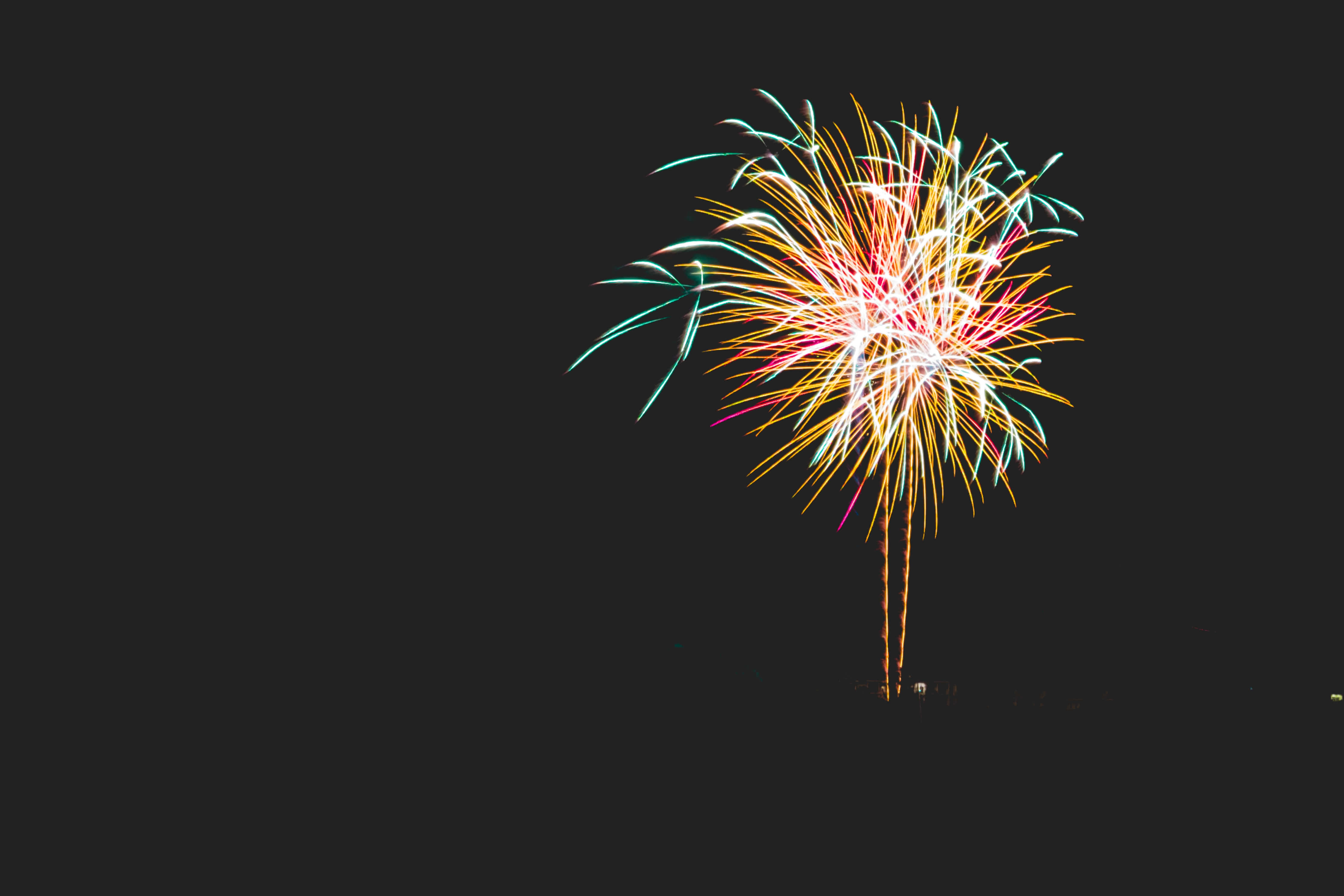 New Year 桌布 壁紙 — 一場充滿活力的煙火爆炸，在漆黑的夜空中綻放出黃色、粉紅色和藍綠色的條紋。
