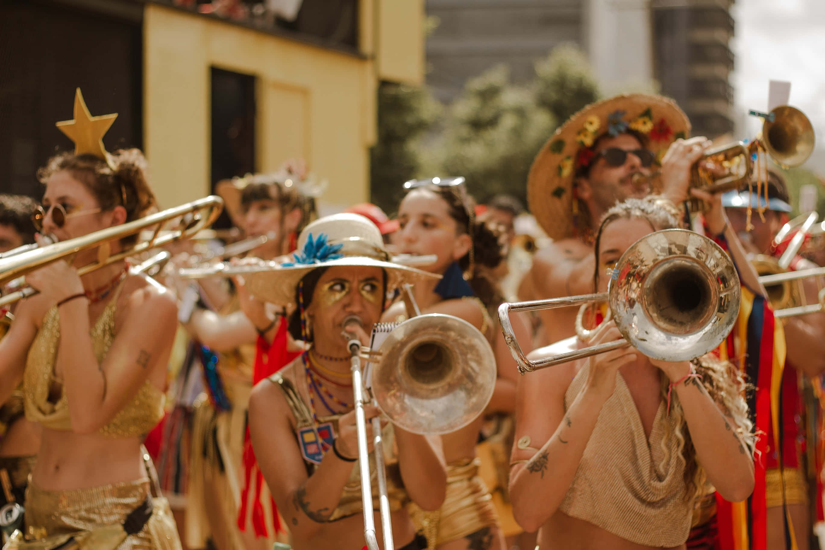 music festival 桌布 壁紙 — 一場充滿活力的街頭遊行，身穿金色服裝的音樂家在明亮的日光下演奏長號和小號。