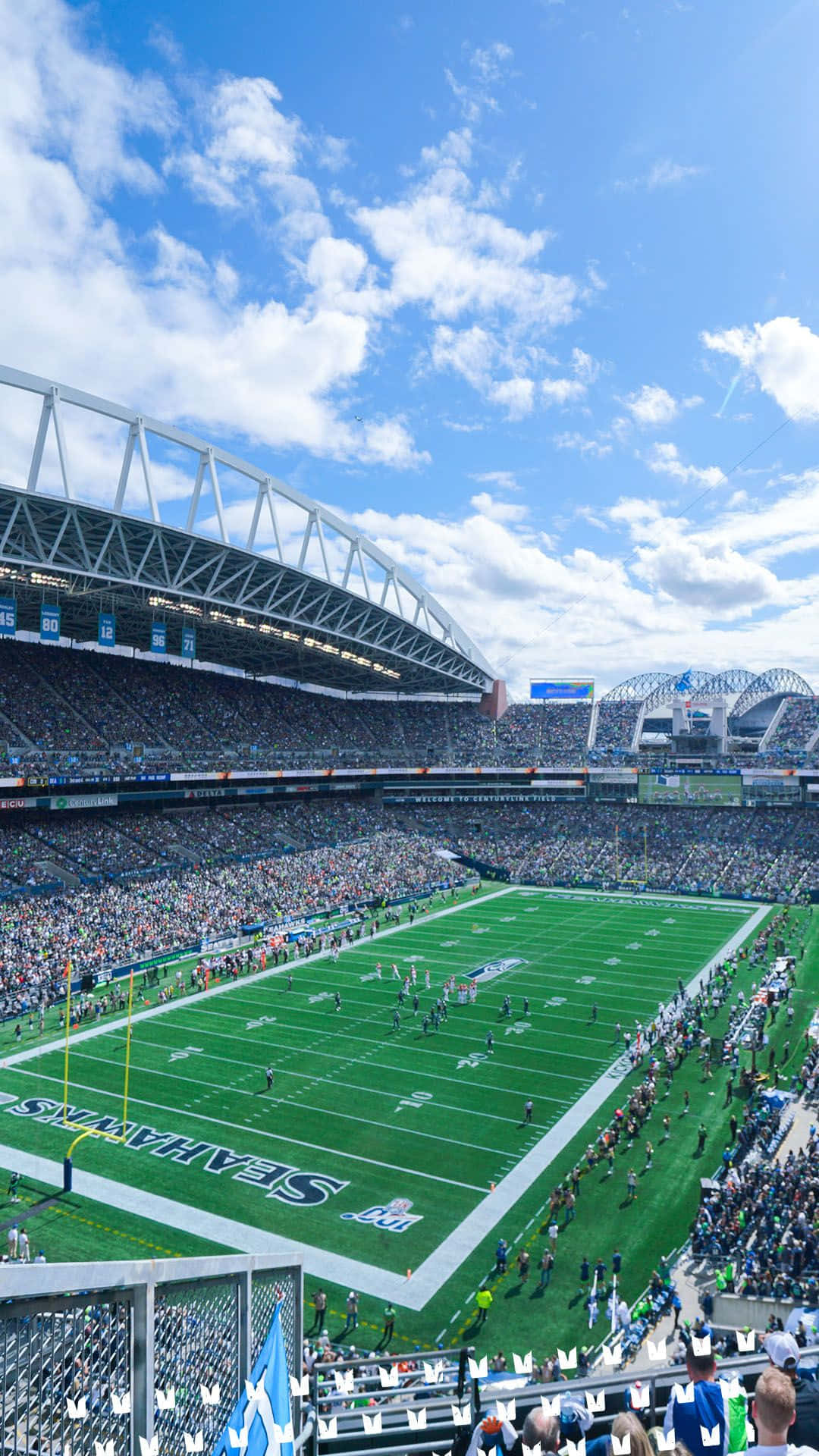 Seattle Seahawks 桌布 壁紙 — 一場充滿活力的足球比賽在晴朗藍天和蓬鬆白雲下，於座無虛席的體育場內展開。