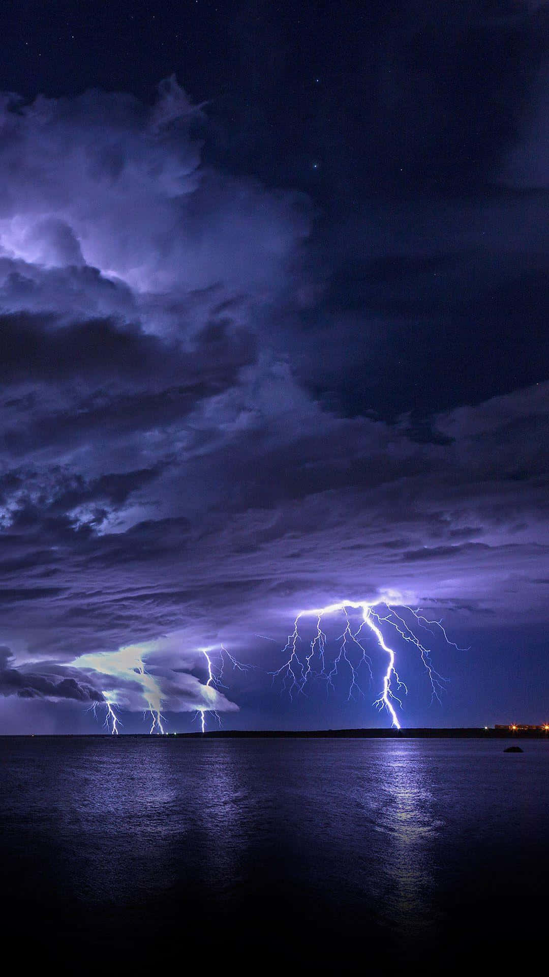 Lightning iPhone 桌布 壁紙 — 一場戲劇性的夜間暴風雨掠過平靜的湖面，生動的紫色閃電照亮烏雲並倒映在水中。