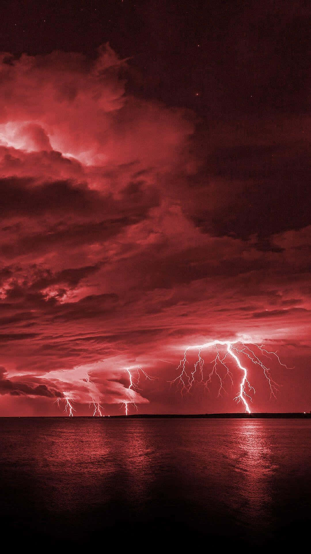 雲朵 桌布 壁紙 — 一場戲劇性的紅色閃電風暴照亮了夜晚平靜反射水面上的黑暗天空。