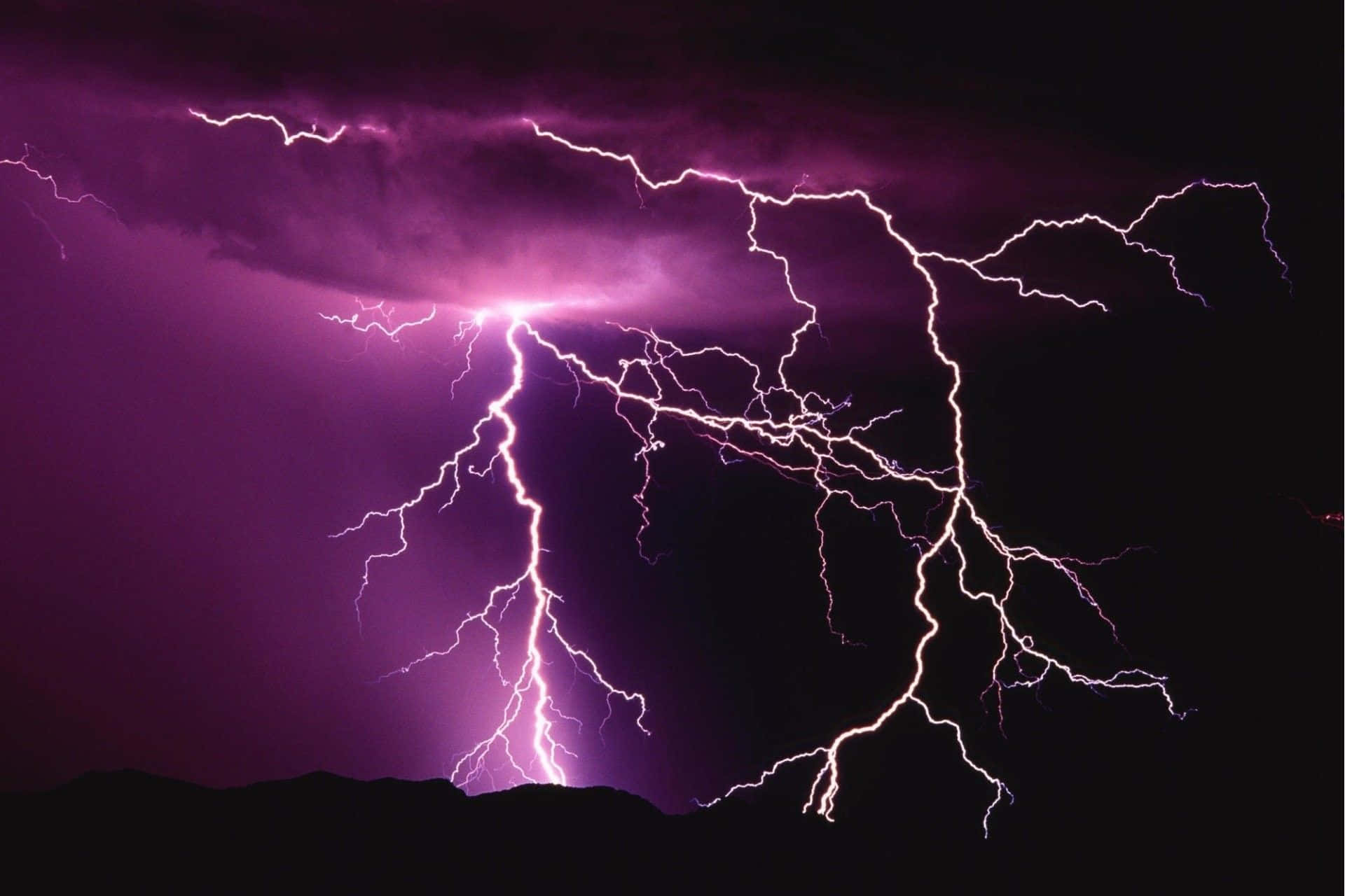 thunder 桌布 壁紙 — 一場戲劇性的紫色閃電風暴照亮了鋸齒狀山脈輪廓上方的黑暗天空。