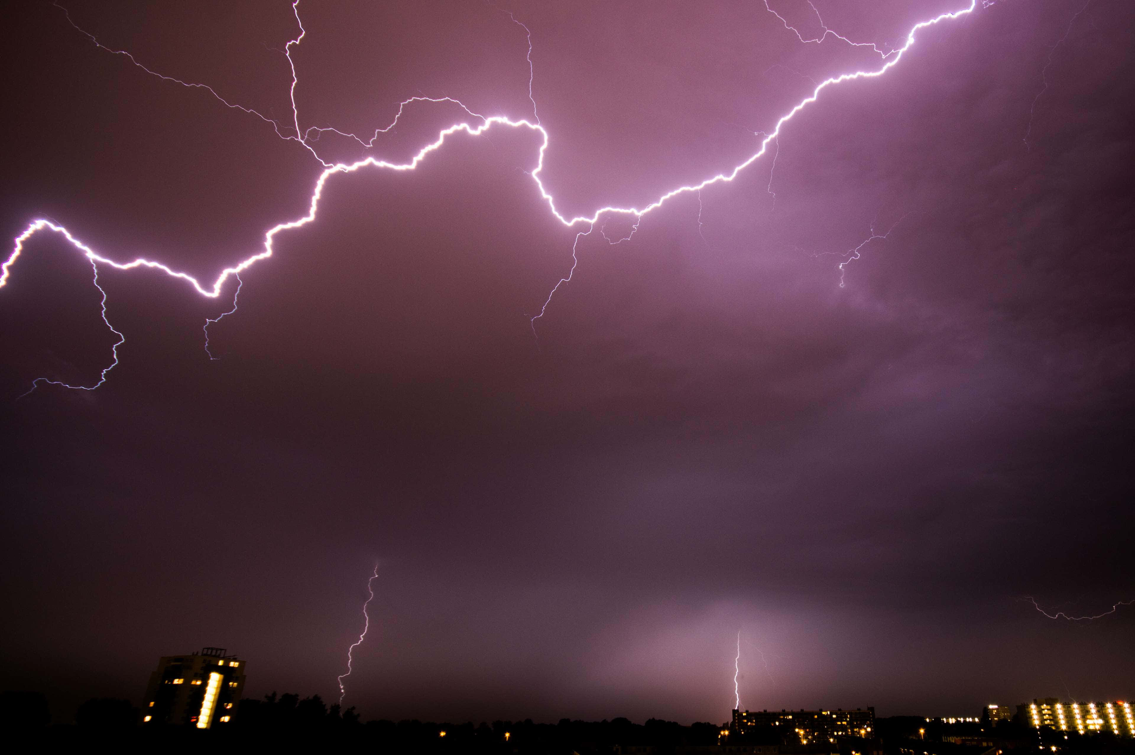 Thunderstorm 桌布 壁紙 — 一場戲劇性的紫色閃電風暴照亮了黑暗的城市天際線，鋸齒狀的閃電劃破夜空。