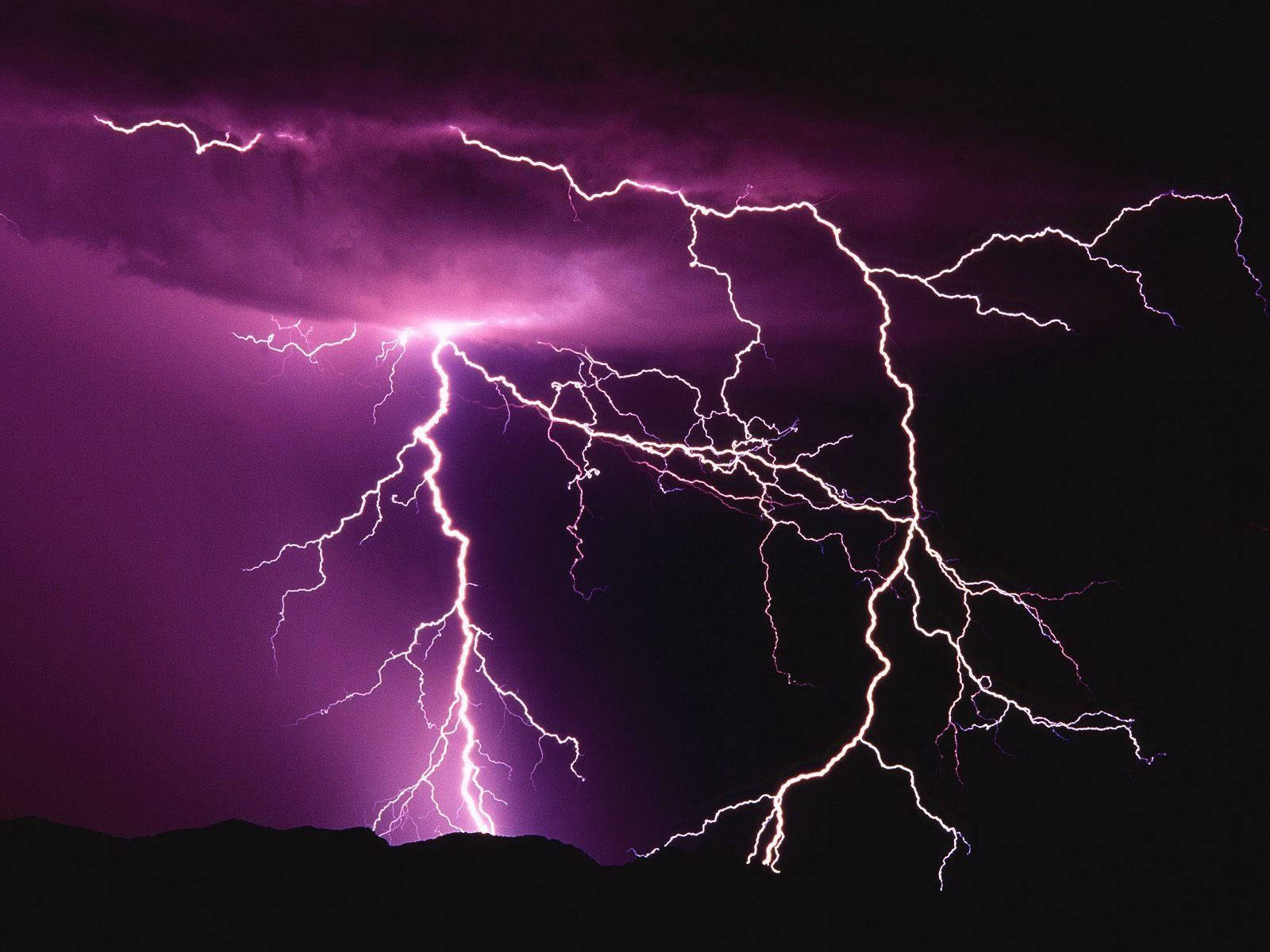 Aesthetic Lightning 桌布 壁紙 — 一場戲劇性的紫色閃電風暴照亮了黑暗的天空，背景是輪廓分明的山脈。