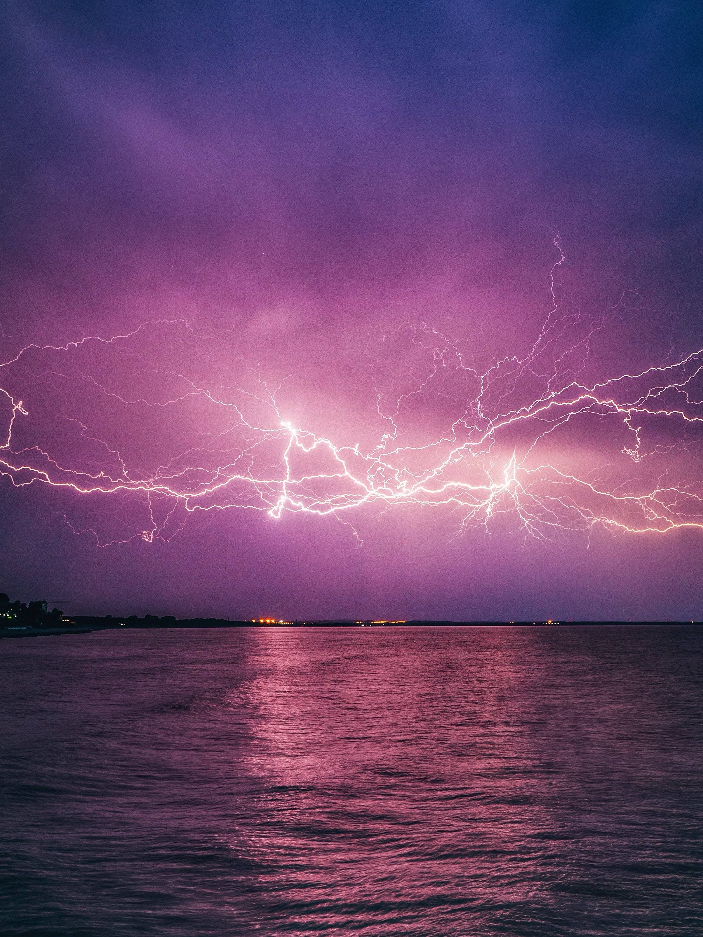 海洋 桌布 壁紙 — 一場戲劇性的紫色雷暴在夜間用生動的電光閃爍照亮平靜的水面。