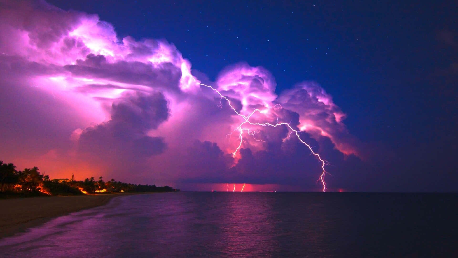 閃電 桌布 壁紙 — 一場戲劇性的紫色雷暴照亮了夜晚的黑暗海洋，伴隨著發光的雲層和遠處的海岸燈光。