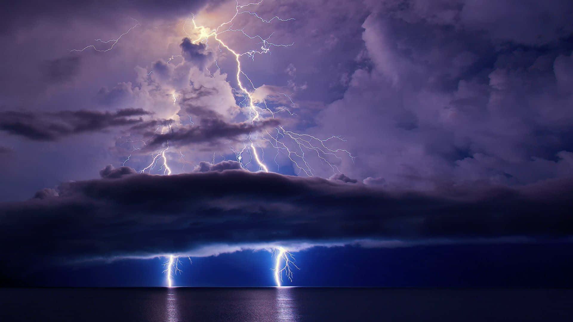 Thunderstorm 桌布 壁紙 — 一場戲劇性的閃電風暴照亮了黑暗的海洋，在動盪的紫色天空下，多道明亮的閃電擊中水面。