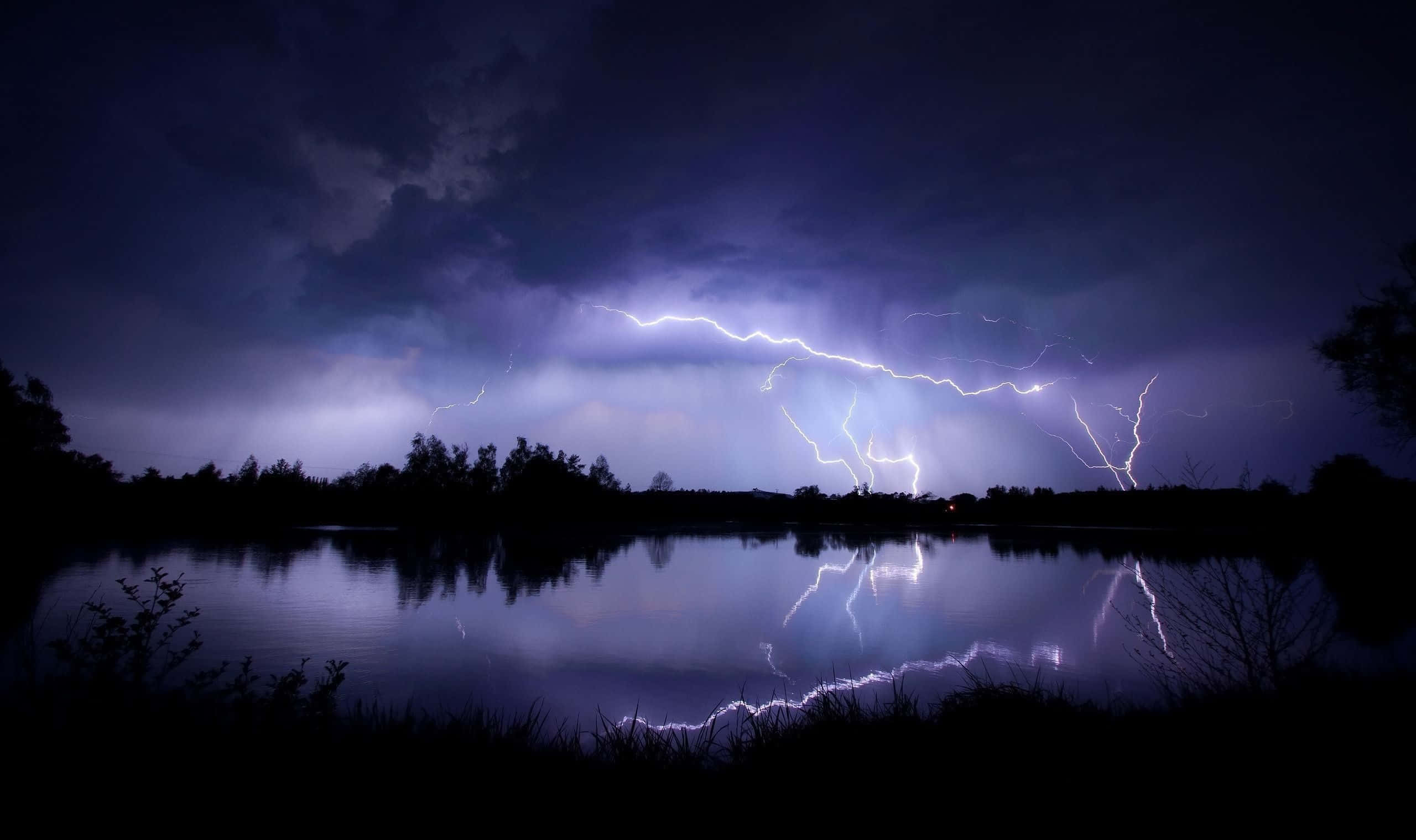 Lightning Bolt 桌布 壁紙 — 一場戲劇性的雷暴照亮了夜晚的黑暗湖泊，紫色和白色的閃電在水中反射出鮮明的光芒。
