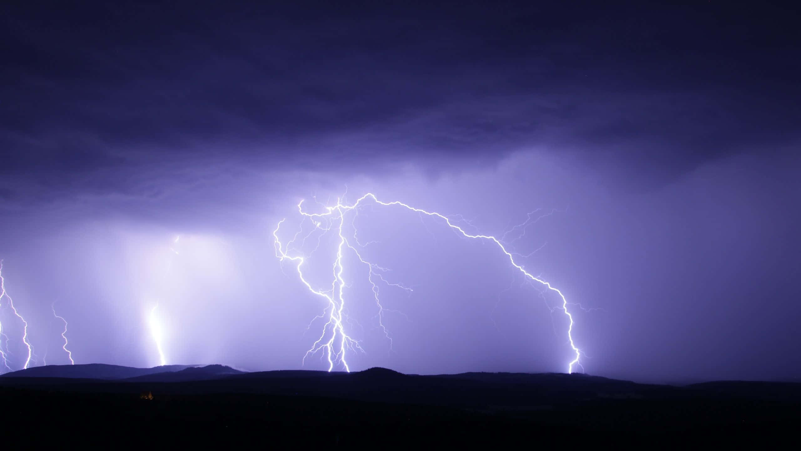 Thunderstorm 桌布 壁紙 — 一場戲劇性的雷暴照亮了夜間剪影山脈上方的深紫色天空。