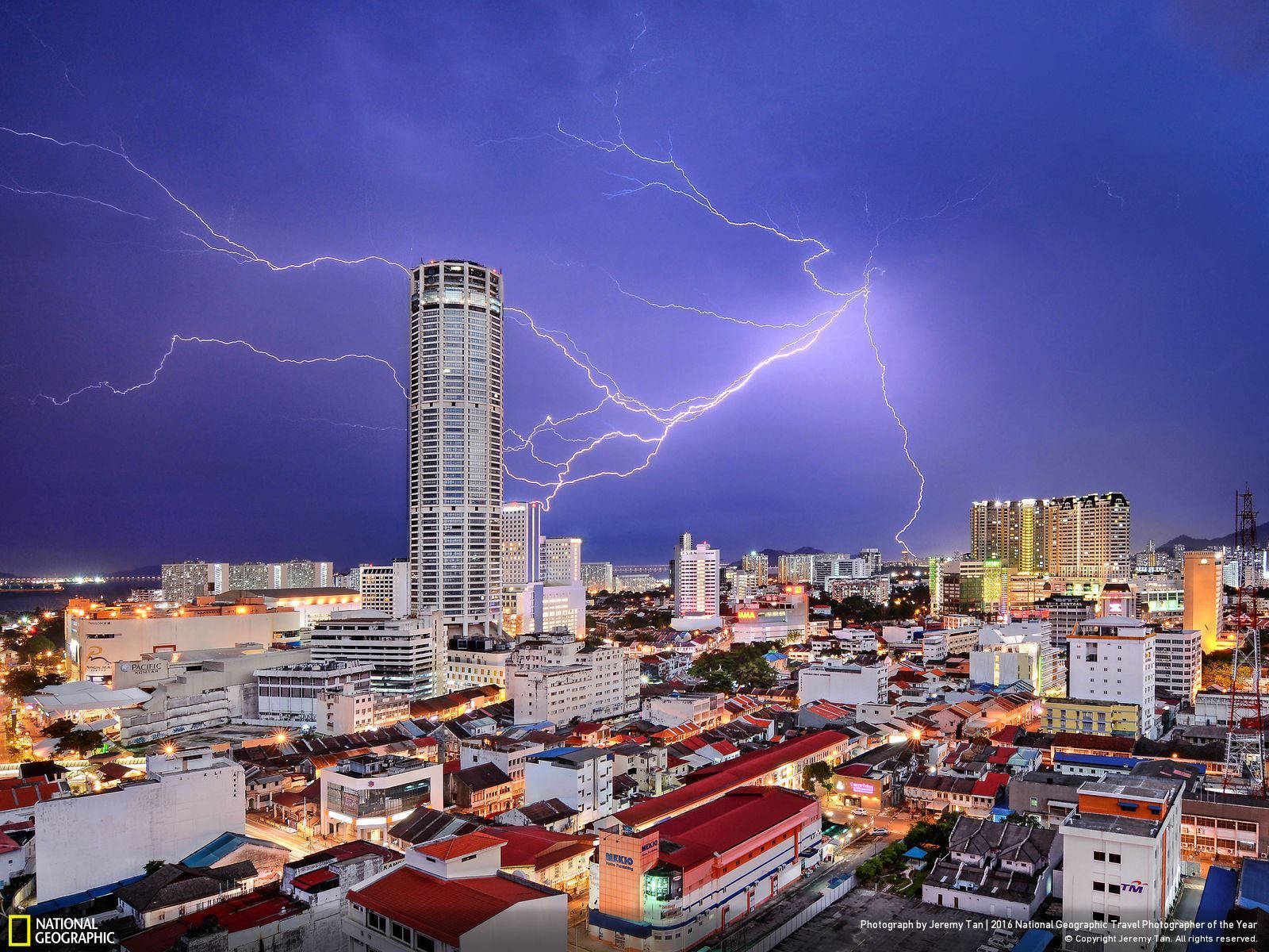 Malaysia 桌布 壁紙 — 一場戲劇性的雷暴照亮了廣闊的城市景觀，高聳的摩天大樓和發光的街燈映襯著深紫色的天空。