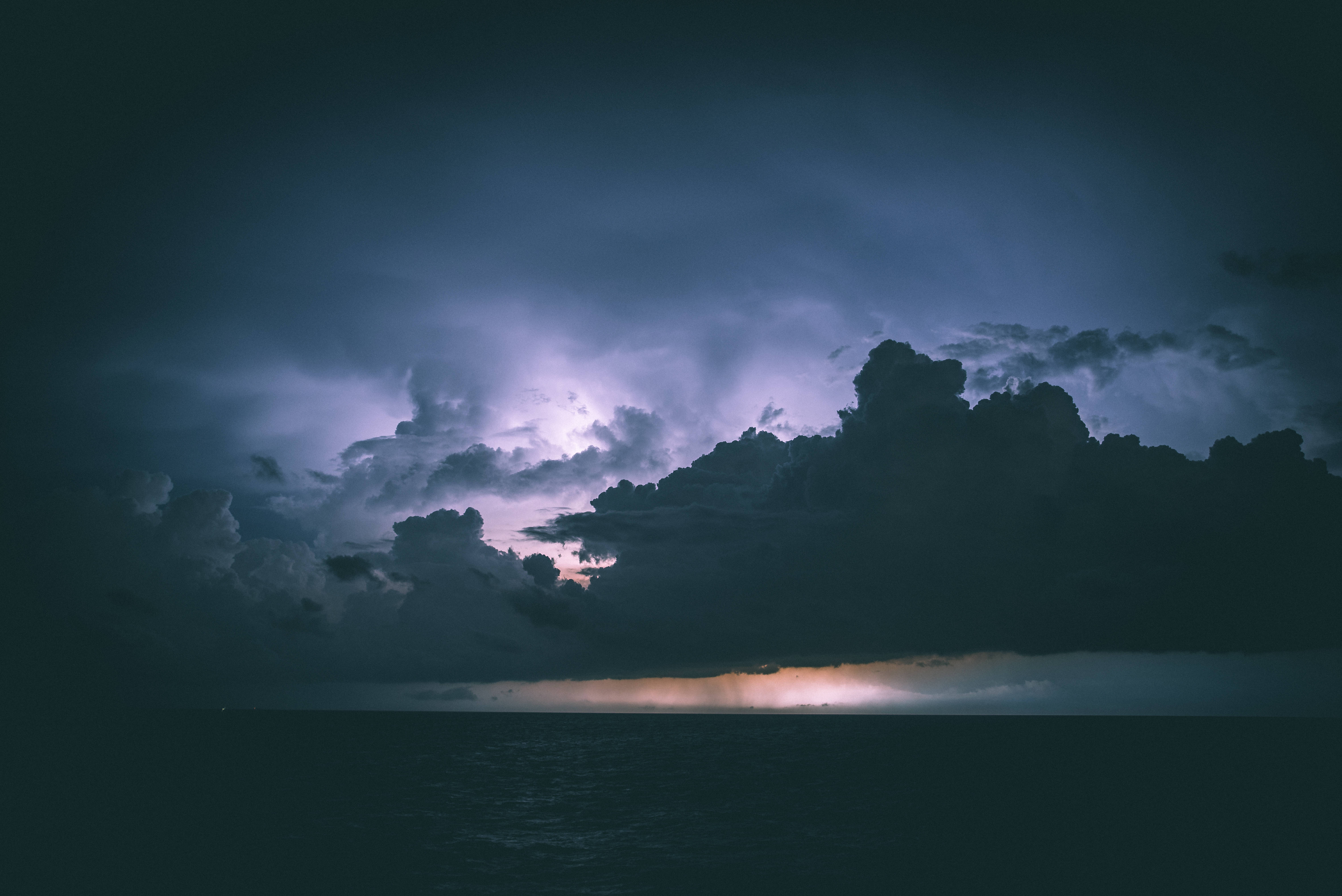 暴風 桌布 壁紙 — 一場戲劇性的風暴在海洋上空，閃電照亮了烏雲和發光的地平線。