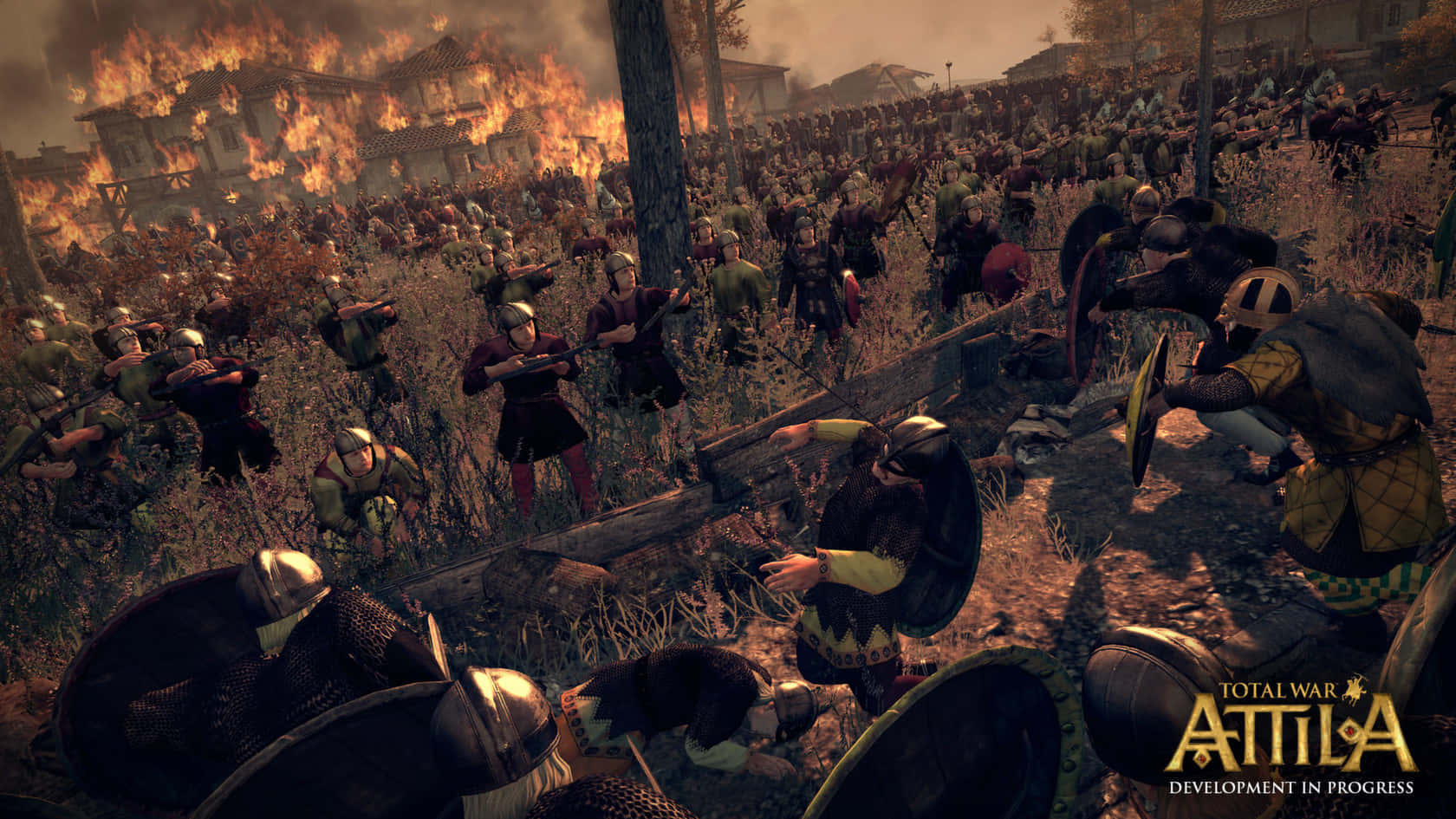 Total War Attila 桌布 壁紙 — 一場混亂的中世紀戰役正在進行，身穿盔甲的戰士在燃燒的木結構建築和煙霧瀰漫的天空中激烈交戰。