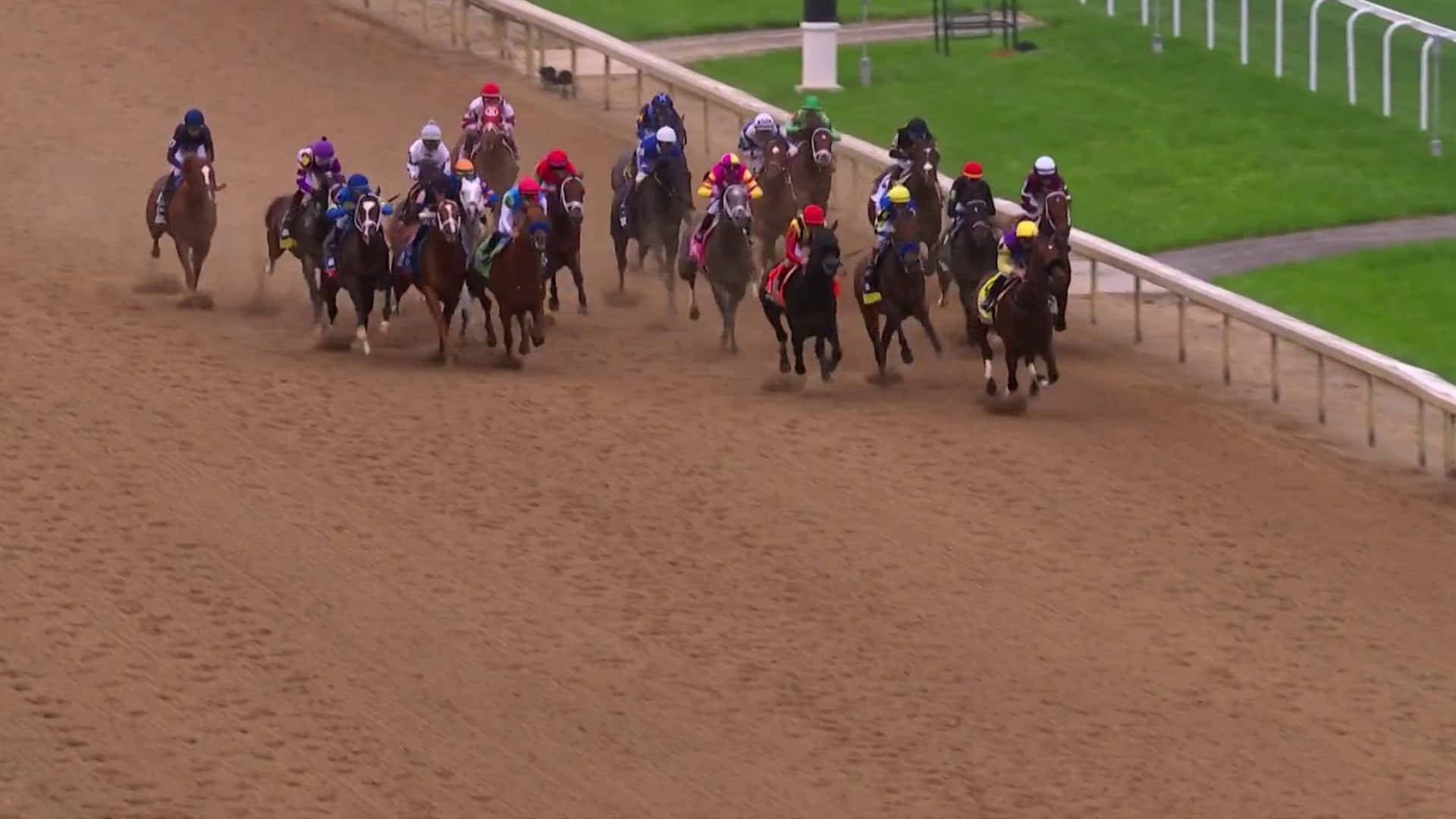 Kentucky Derby 桌布 壁紙 — 一場激動人心的賽馬展開，騎師們身穿色彩繽紛的綵衣，在陽光普照的泥地賽道上策馬前進。