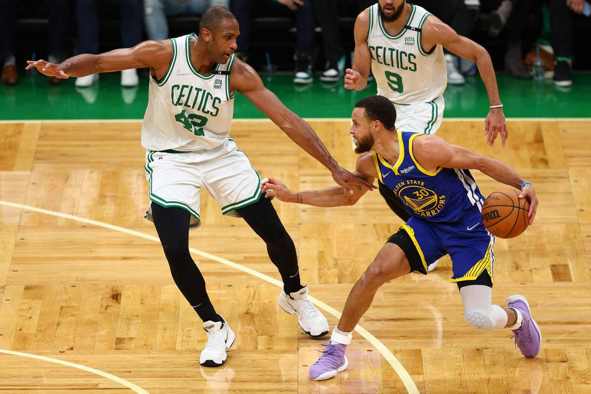 NBA 桌布 壁紙 — 一場激烈的比賽中，一名身穿藍色球衣的籃球運動員運球越過一名身穿白色塞爾提克球衣的防守球員。