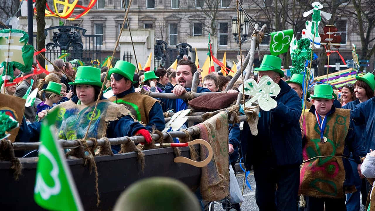St Patrick's Day 桌布 壁紙 — 一場熱鬧的聖派翠克節遊行，人們戴著綠色帽子、穿著手工製作的服裝，在城市的街道上行進。
