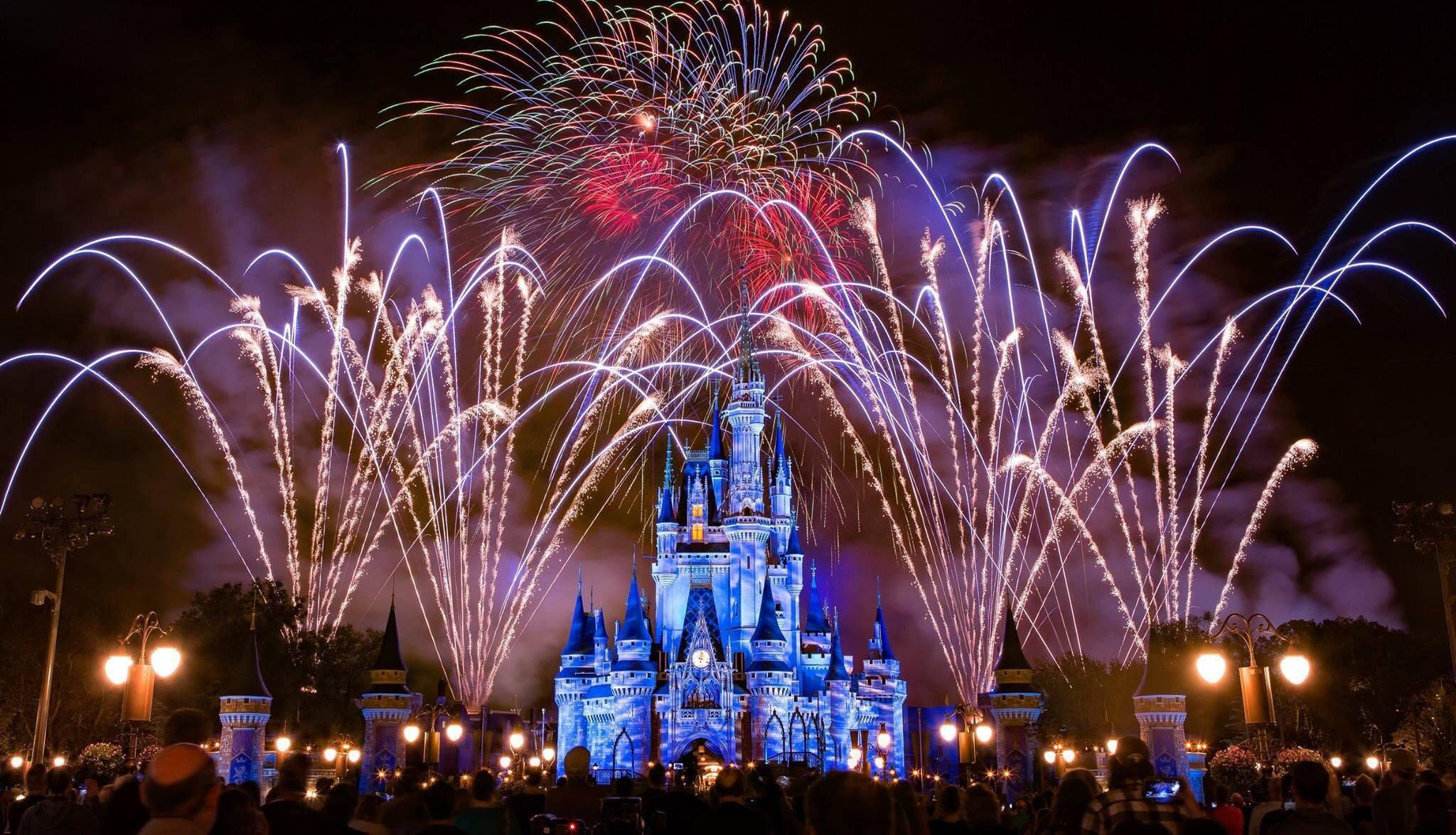 Disney Castle 桌布 壁紙 — 一場絢麗的煙火表演在夜間於灰姑娘城堡上空綻放，以藍色燈光點亮這座標誌性建築，並在黑暗的天空中投射出鮮豔的條紋。