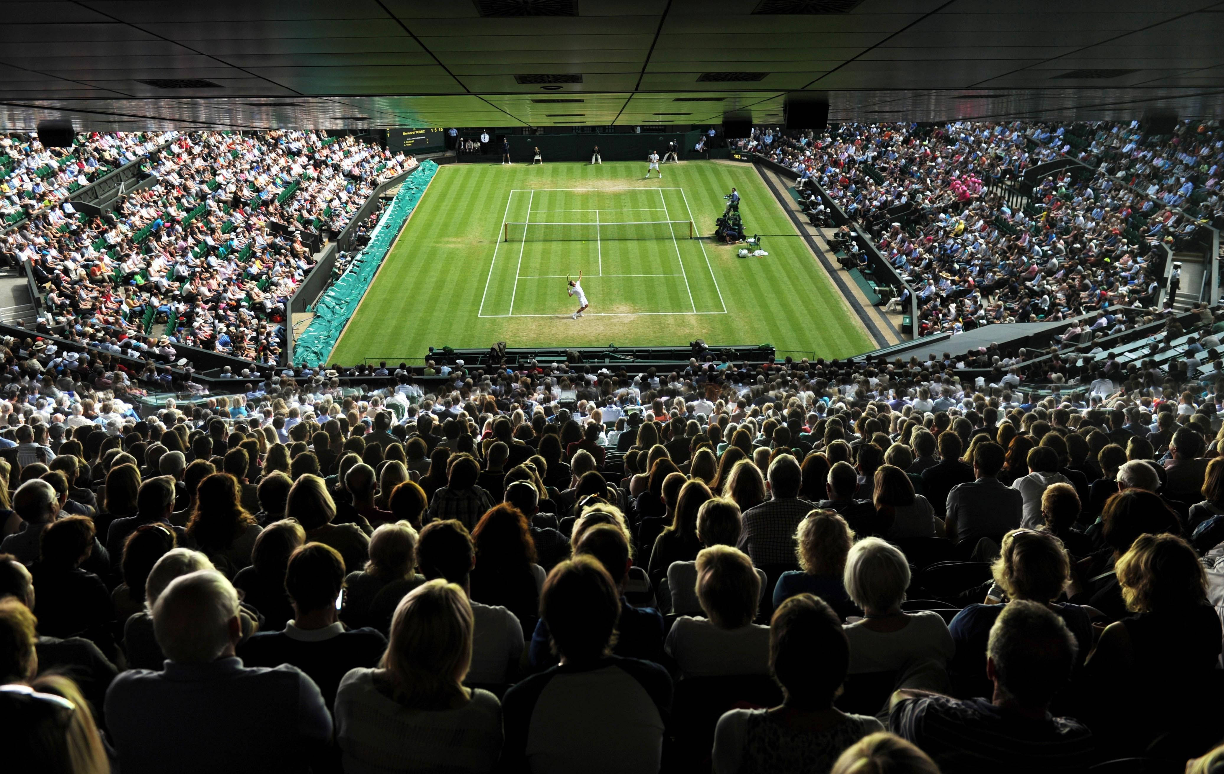 Wimbledon 桌布 壁紙 — 一場網球比賽在體育館燈光下的草地網球場展開，滿座的觀眾從階梯式座位專注觀看。