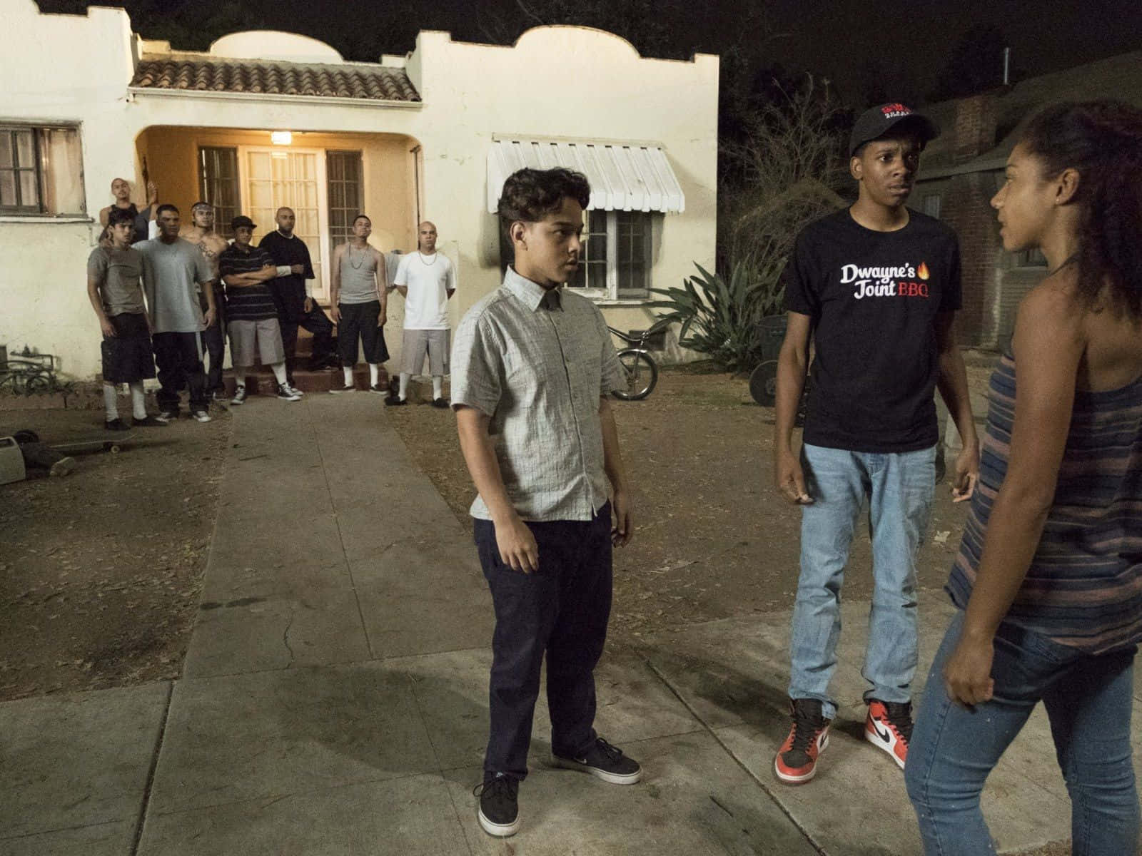 Celebrity 桌布 壁紙 — 一場緊張的夜間對峙在住宅區人行道上展開，青少年在街燈下對峙，背景是一棟房子。