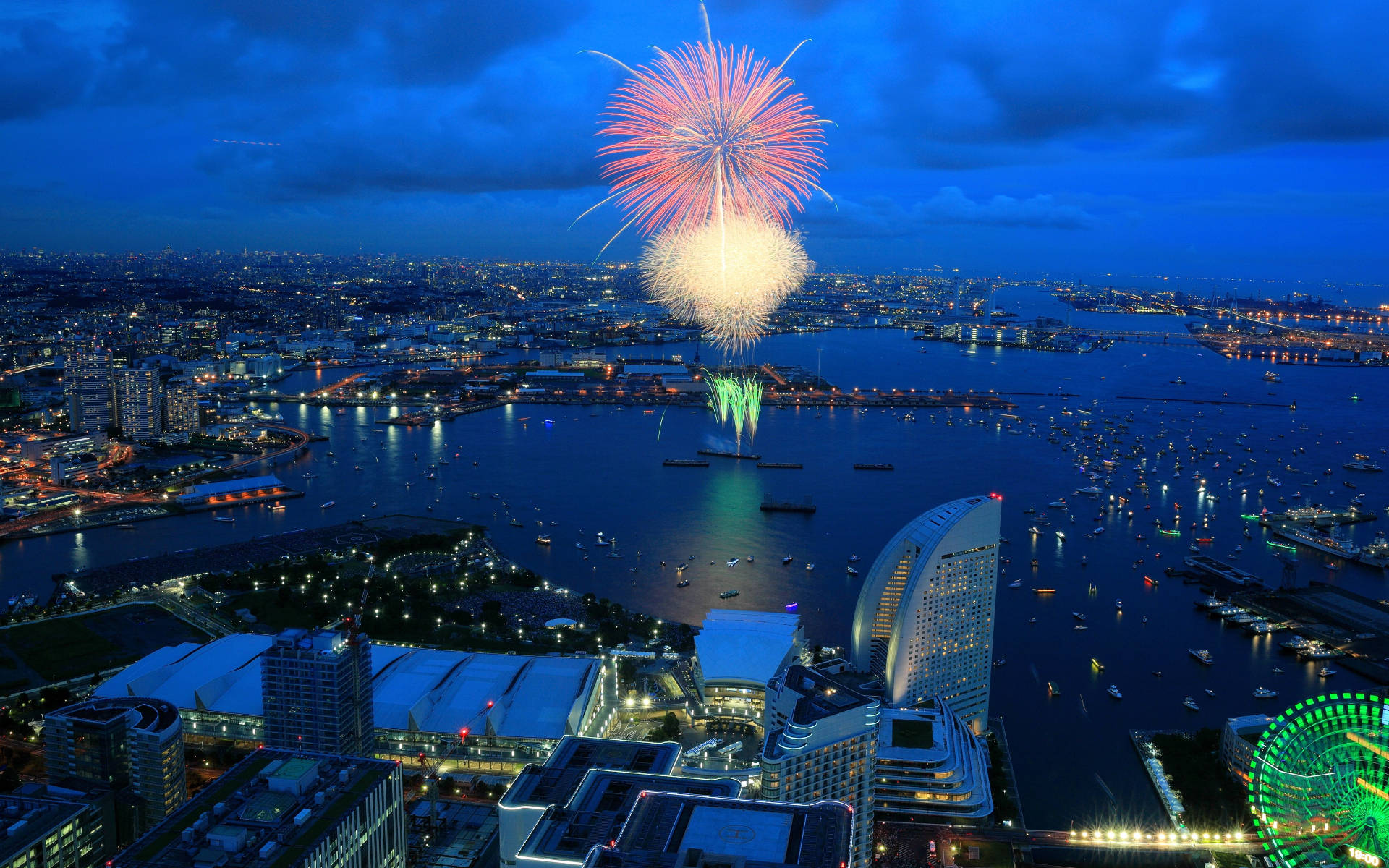 Yokohama 桌布 壁紙 — 一場耀眼的煙火爆炸照亮了暮色天空，下方是閃爍的城市海濱，有船隻和發光的摩天輪。