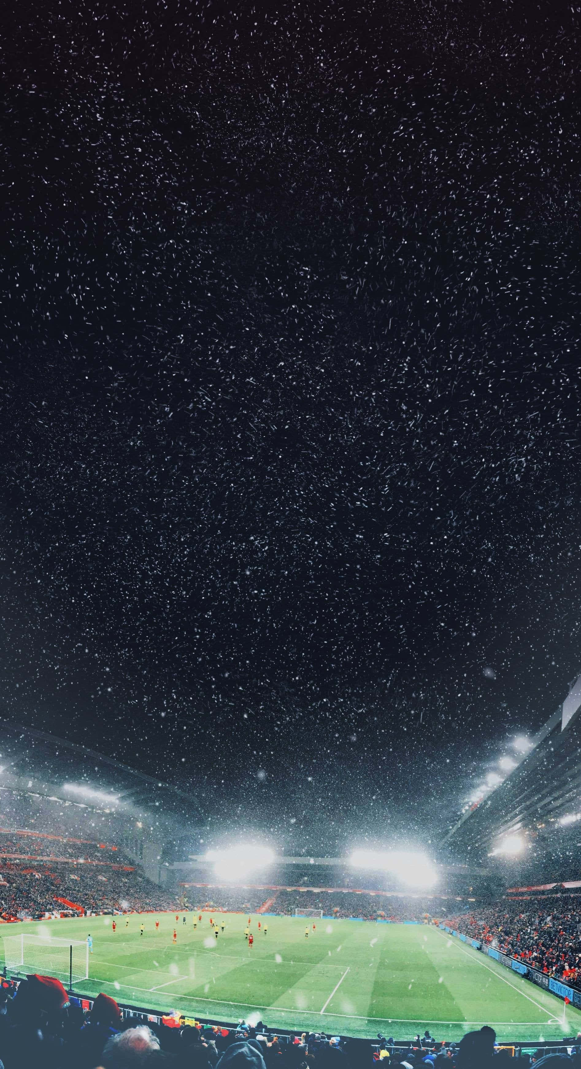 Soccer Aesthetic 桌布 壁紙 — 一場降雪覆蓋了夜晚燈火通明的足球場，球員們在球場燈光下比賽。