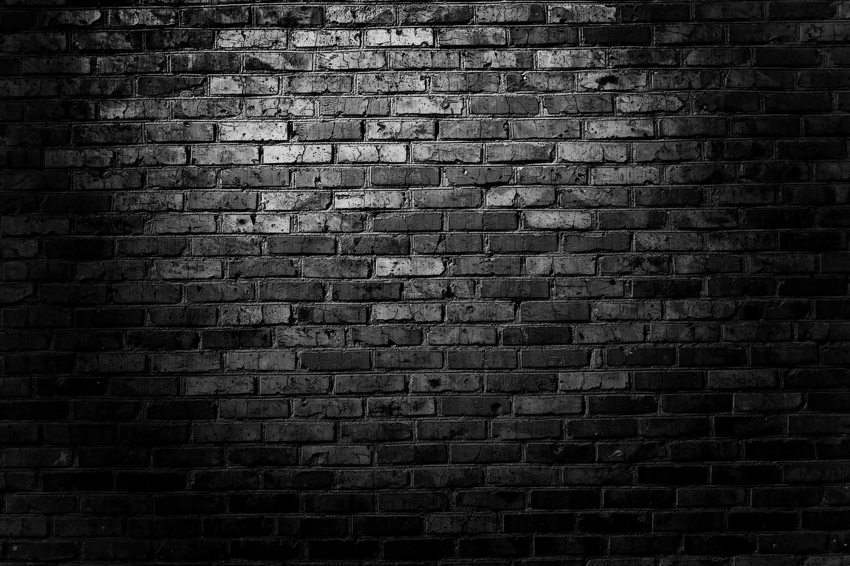 Brick 桌布 壁紙 — 一堵 stark 黑色磚牆，由單一聚光燈照亮，在其紋理表面上投射出戲劇性的陰影。