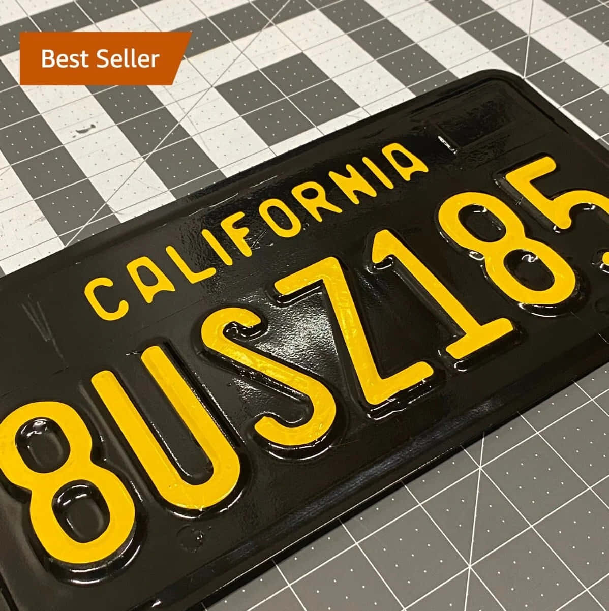 License Plate 桌布 壁紙 — 一塊亮面黑色加州車牌，上面有粗體黃色字母，放在灰白格紋切割墊上。