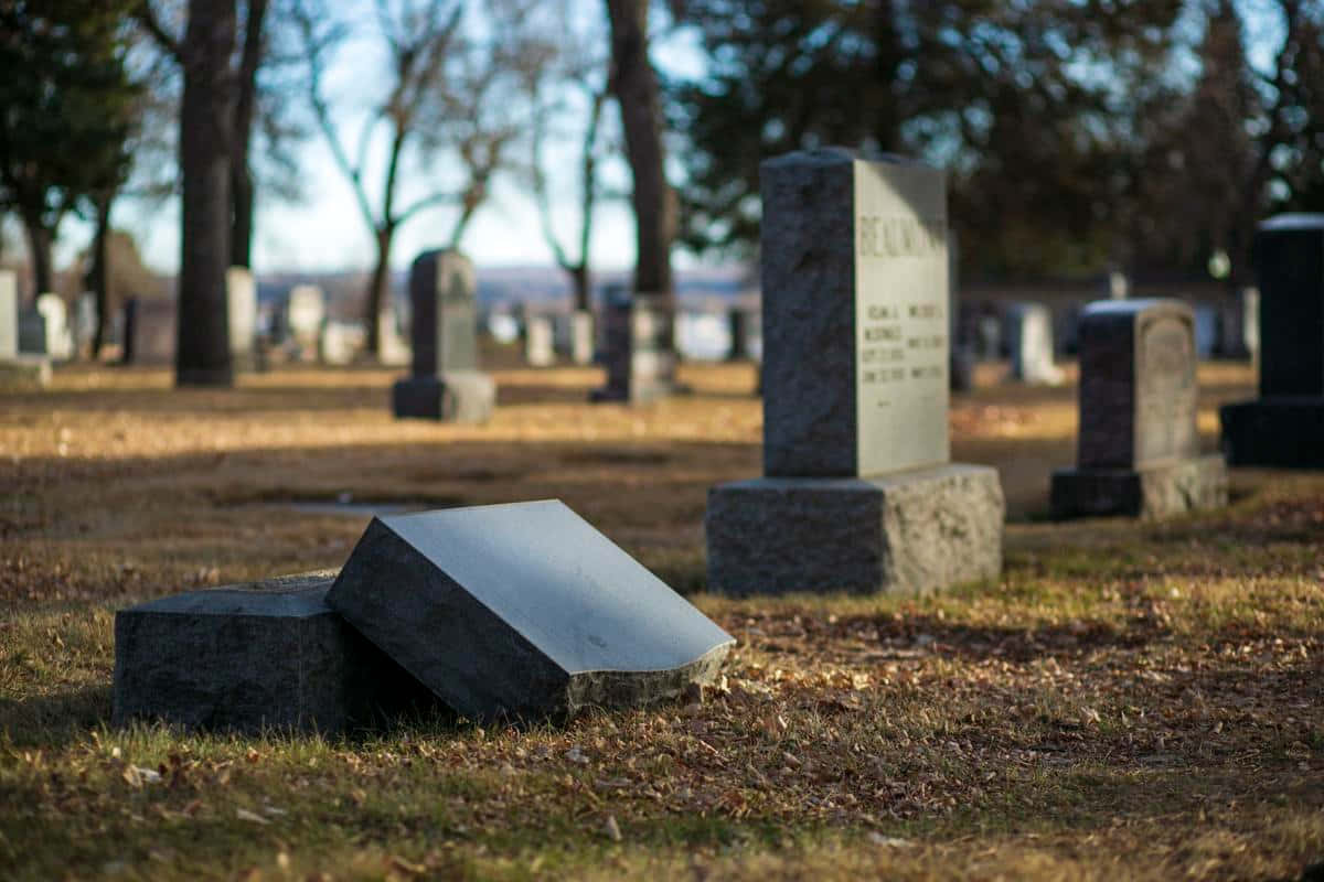 Memorial 桌布 壁紙 — 一塊倒下的墓碑傾斜地躺在一個寧靜的墓園中，周圍有其他直立的墓碑，上方是清澈的藍天。