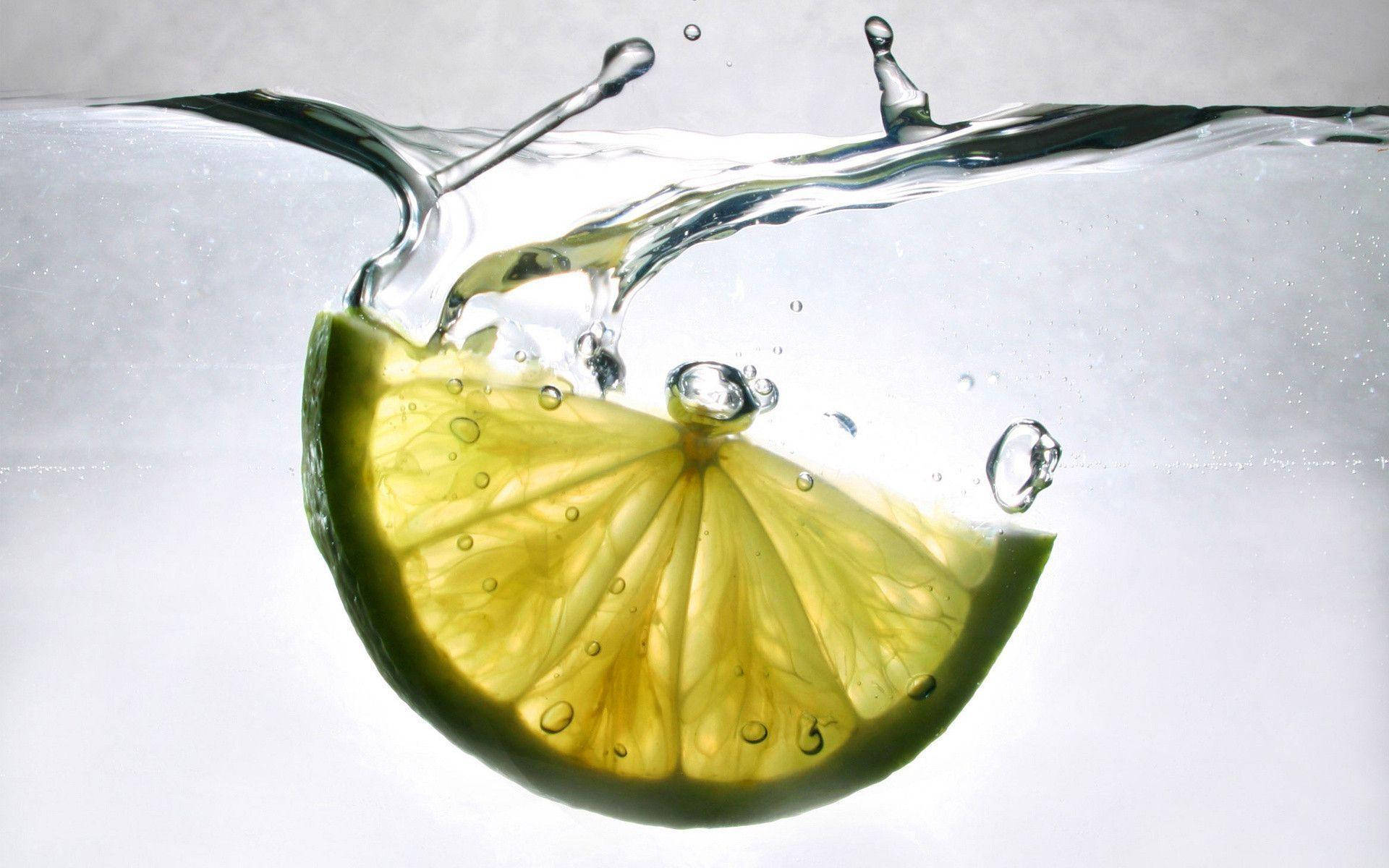 Fruit 桌布 壁紙 — 一塊充滿活力的萊姆片掉入清澈的水中，產生動態的水花和閃閃發光的氣泡。