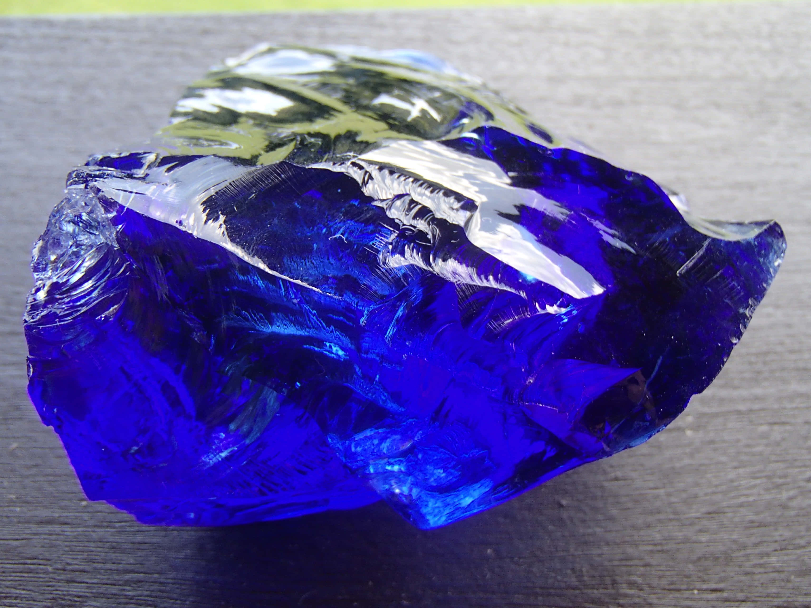 Cobalt Blue 桌布 壁紙 — 一塊充滿活力的鈷藍色玻璃碎片，帶有鋸齒狀邊緣和反射高光，放置在深色木質表面上。
