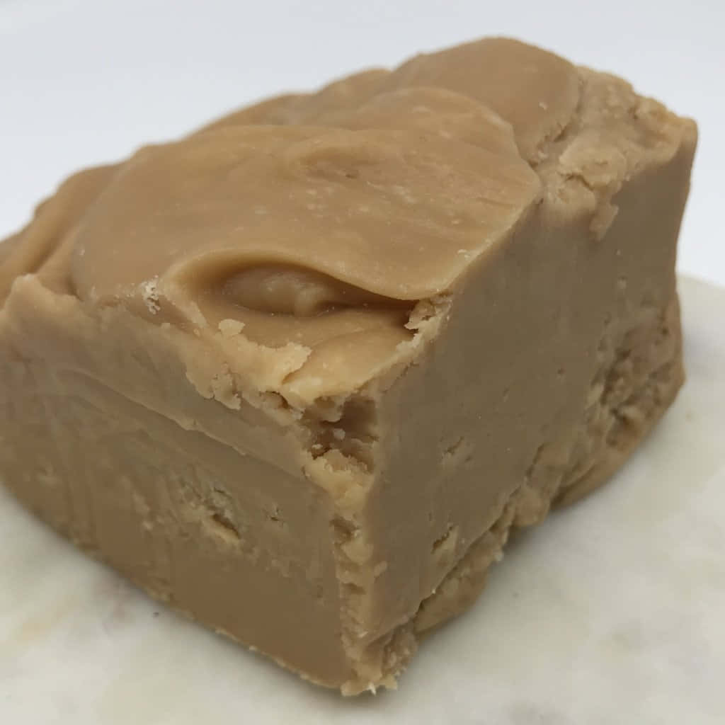 Penuche Fudge 桌布 壁紙 — 一塊光滑焦糖色軟糖方塊的特寫，表面有光澤，邊緣易碎，置於白色大理石表面上。